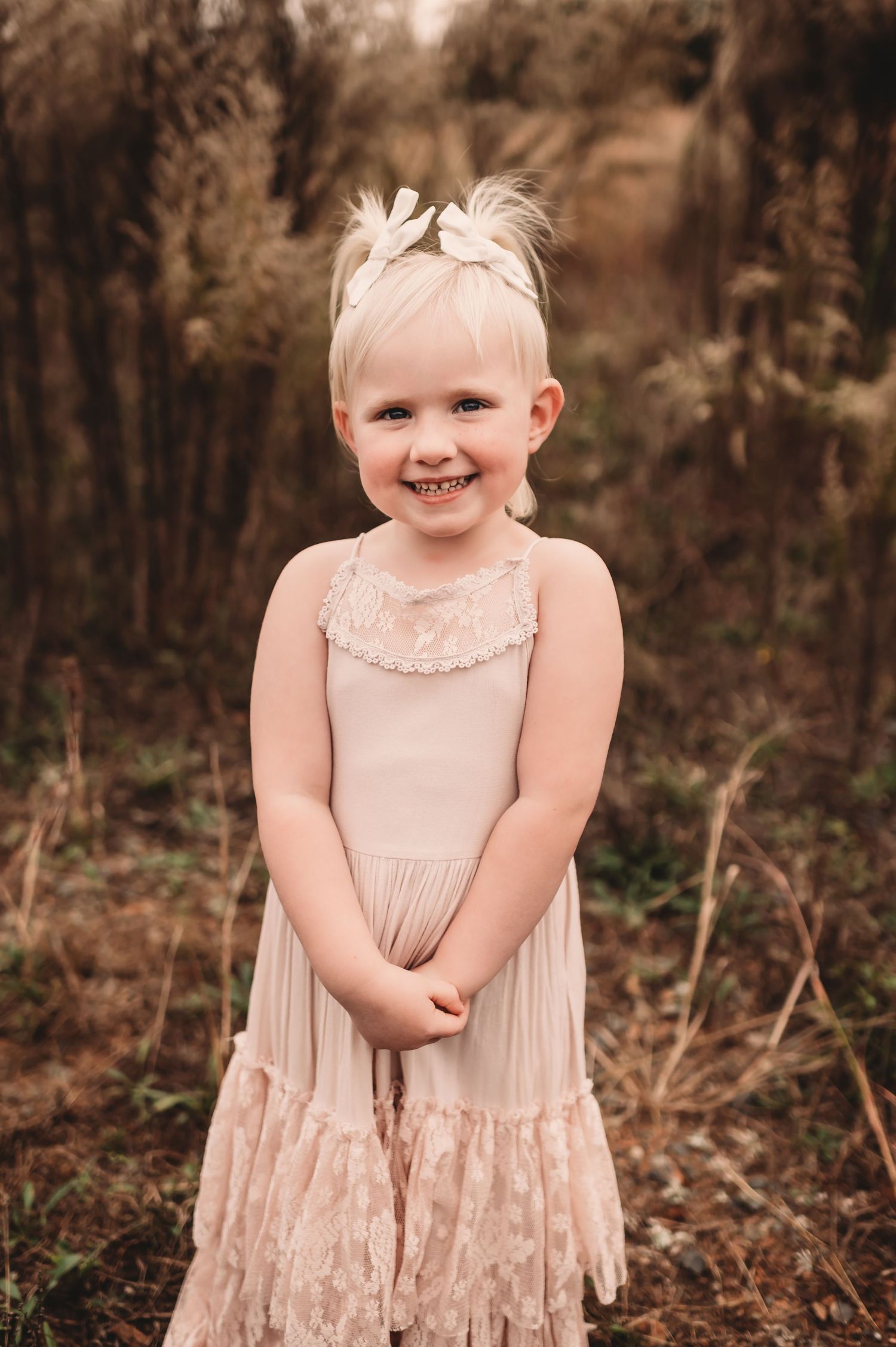 A young girl sweetly smiling at the camera while clasping her hands together.