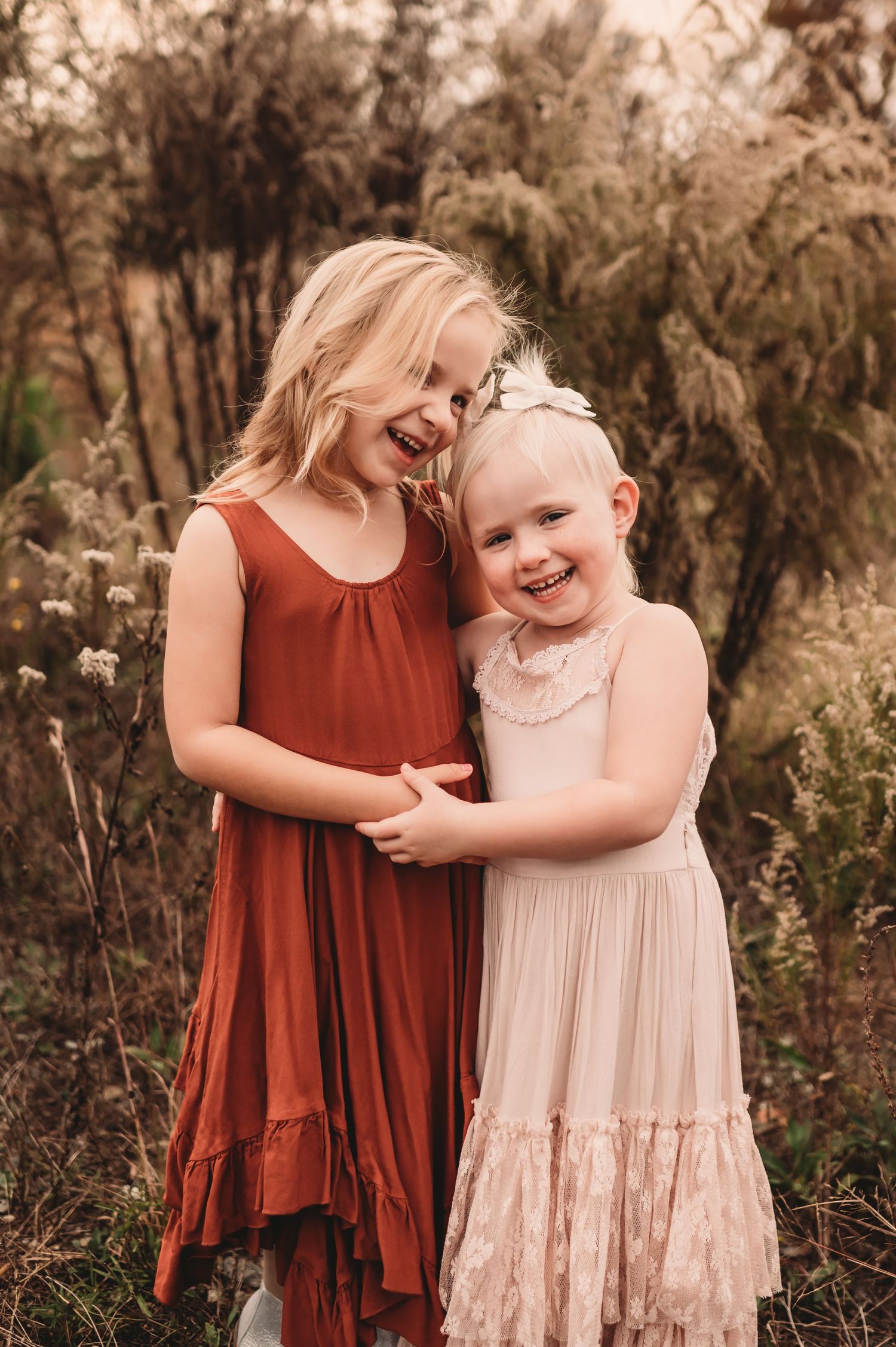 Two young sisters laughing together and holding hands in a tall grass field at Stevens Creek Nature Center in Charlotte, NC.