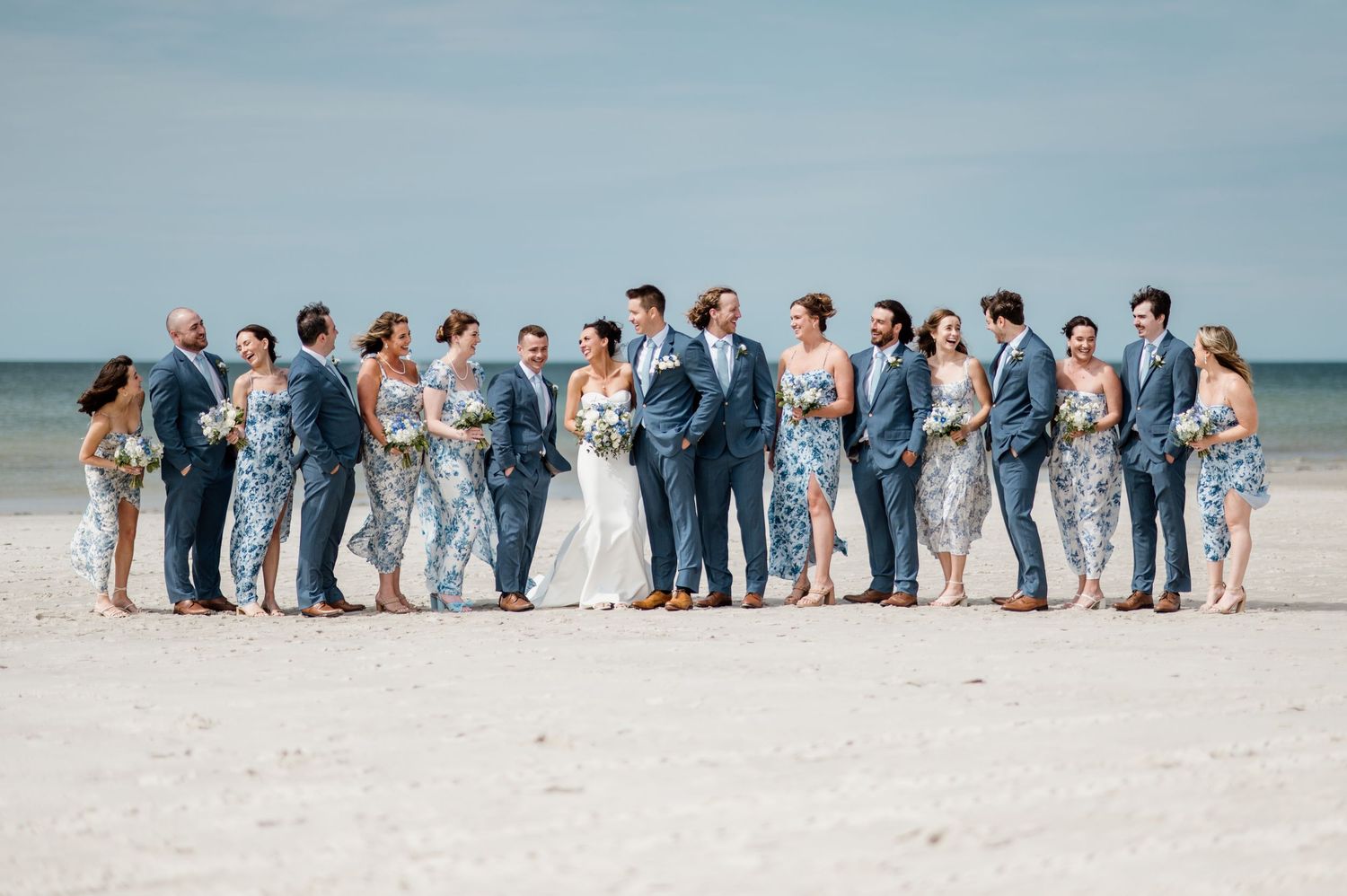 Wedding party lined up on beach wearing blue and white attire.
