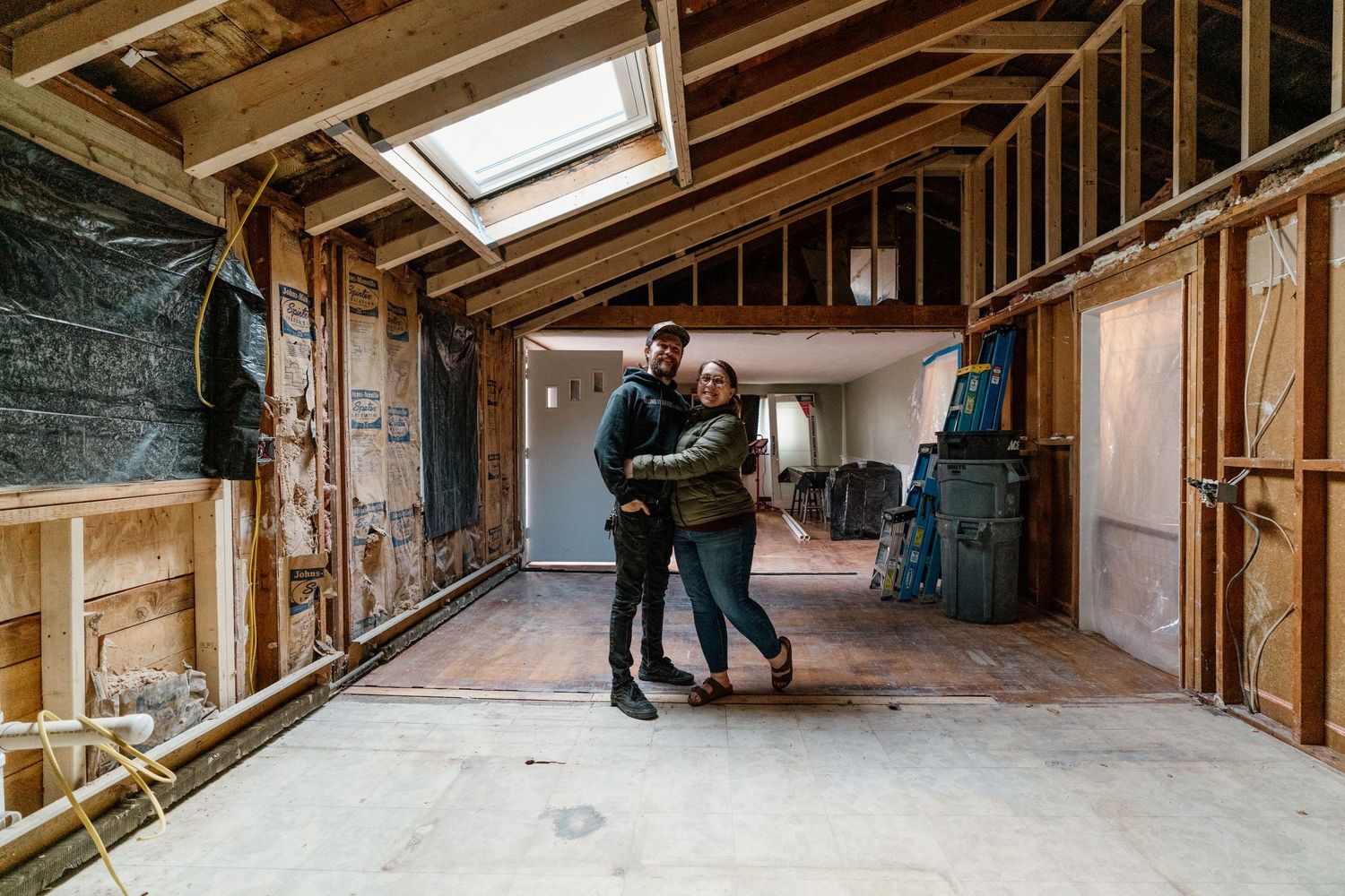 Construction workers inspect exposed wooden framing and insulation in an unfinished attic renovation project.