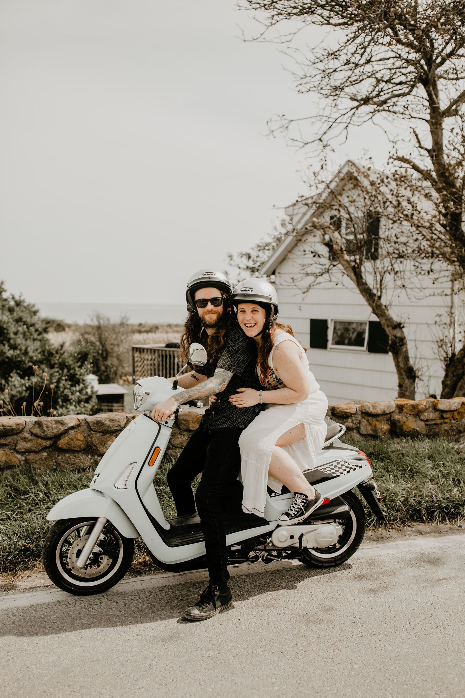 A couple poses together on a white motorcycle in a romantic outdoor photoshoot.