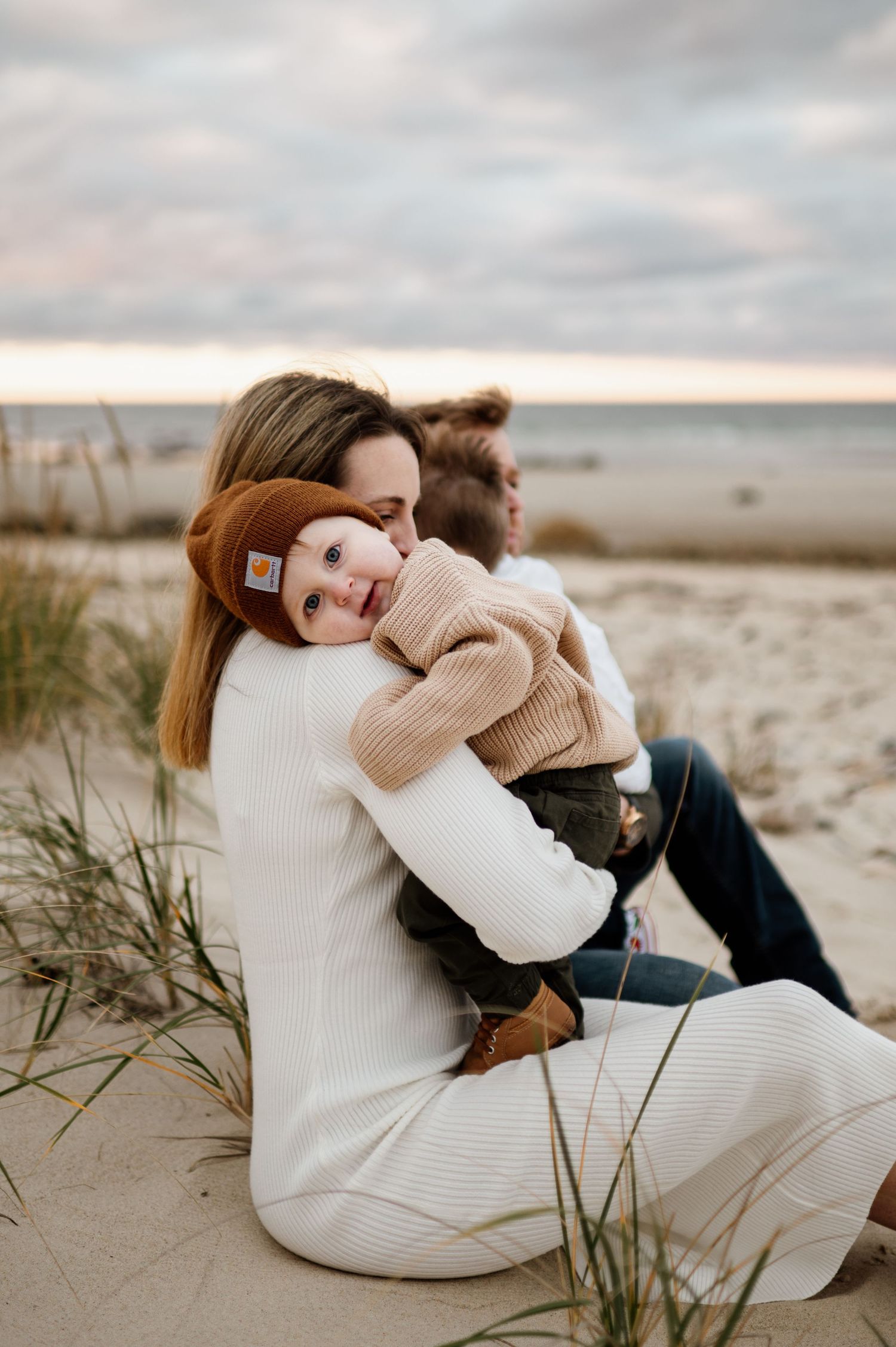 Couple in cozy sweaters sharing tender moments on a sandy beach at sunset.