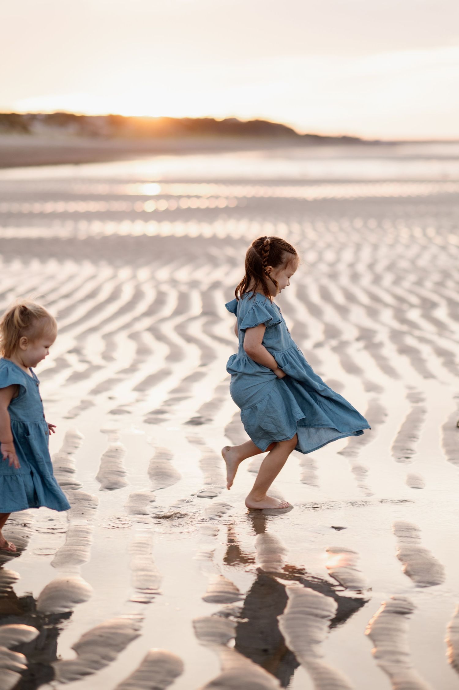 Young child in blue dress running and playing on rippled sand patterns at sunset.