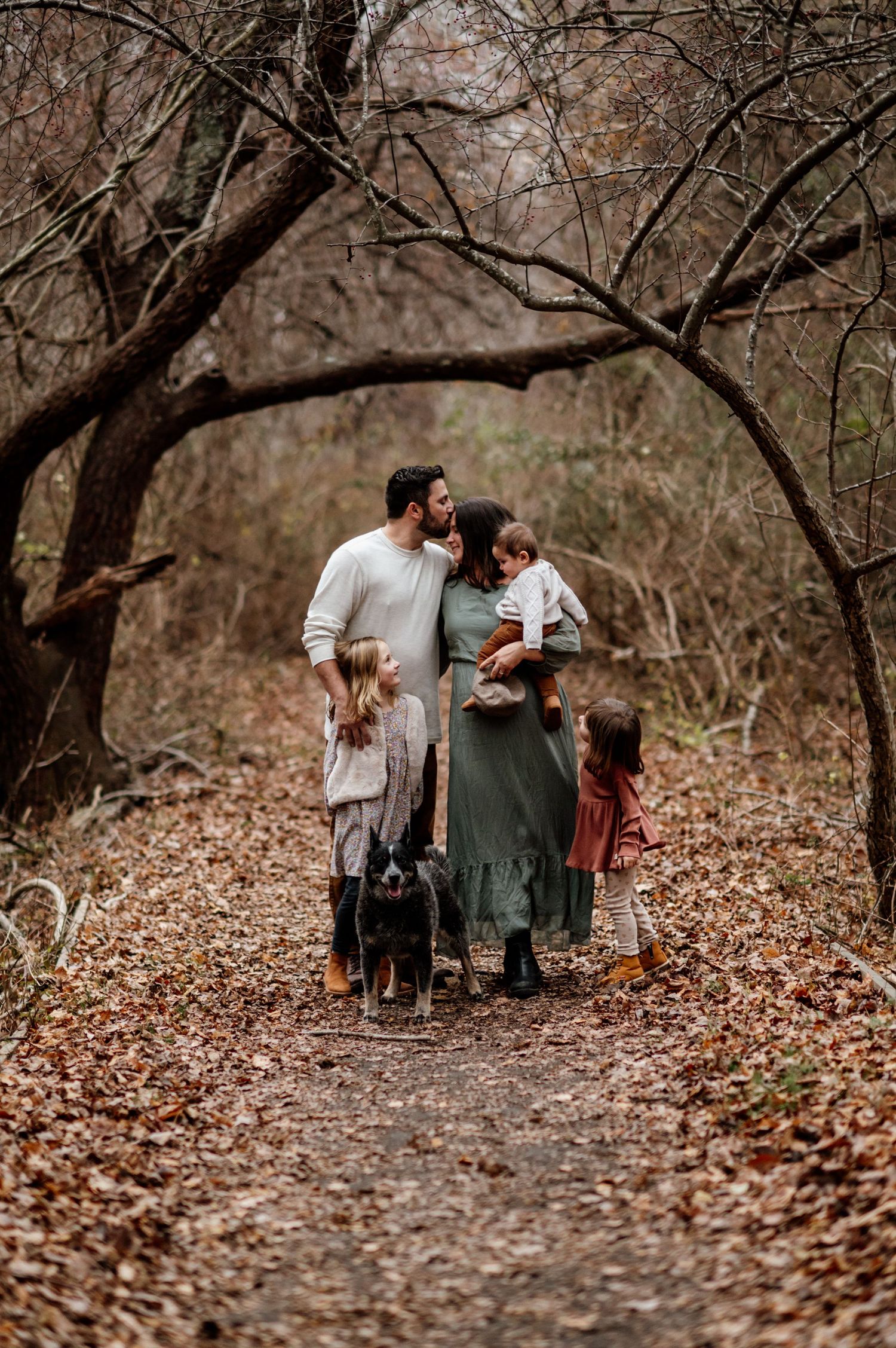 Family walking through a wooded trail covered in fallen autumn leaves.