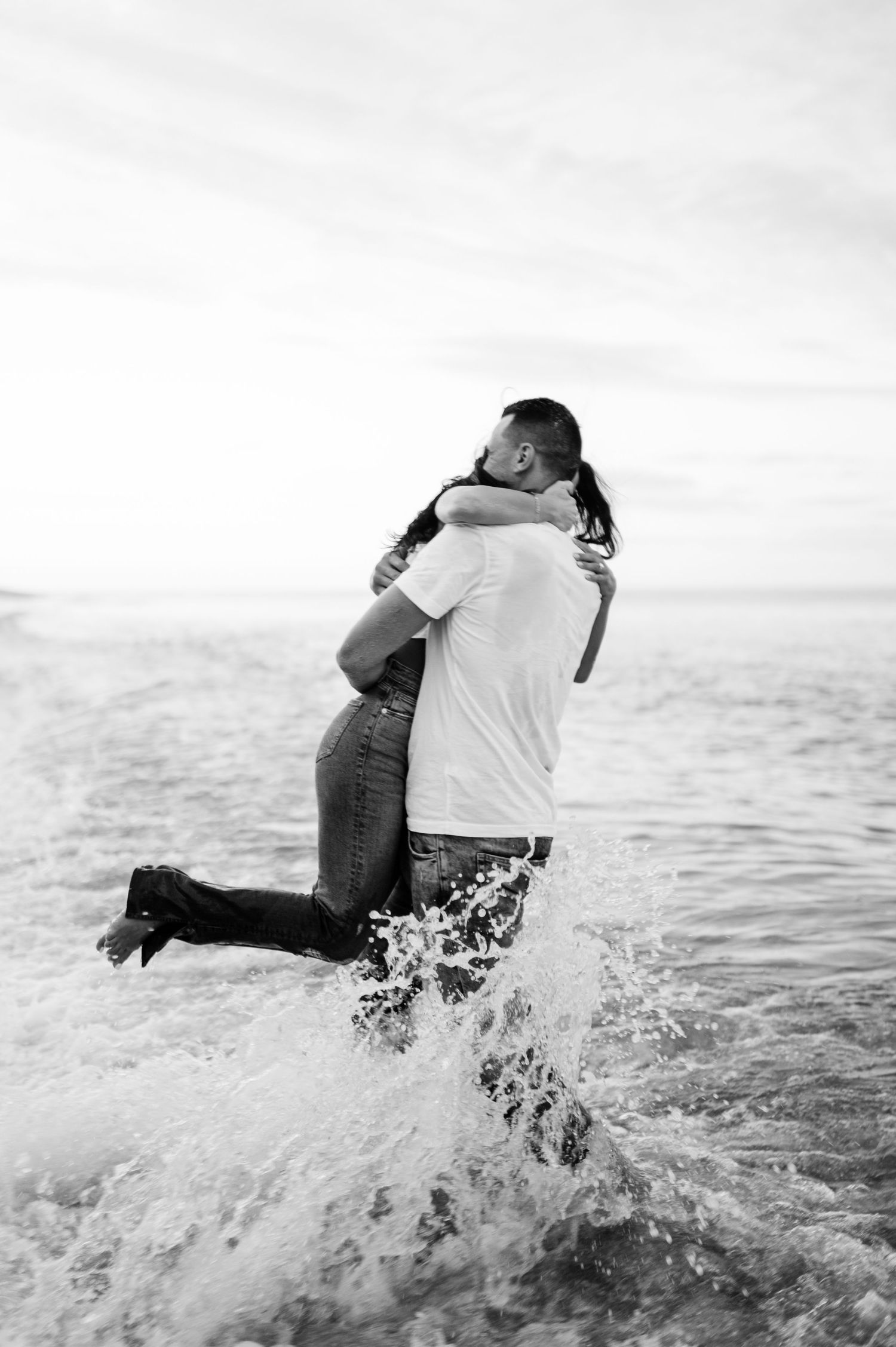 Black and white photo series of couple playing in ocean waves with joyful splashing.
