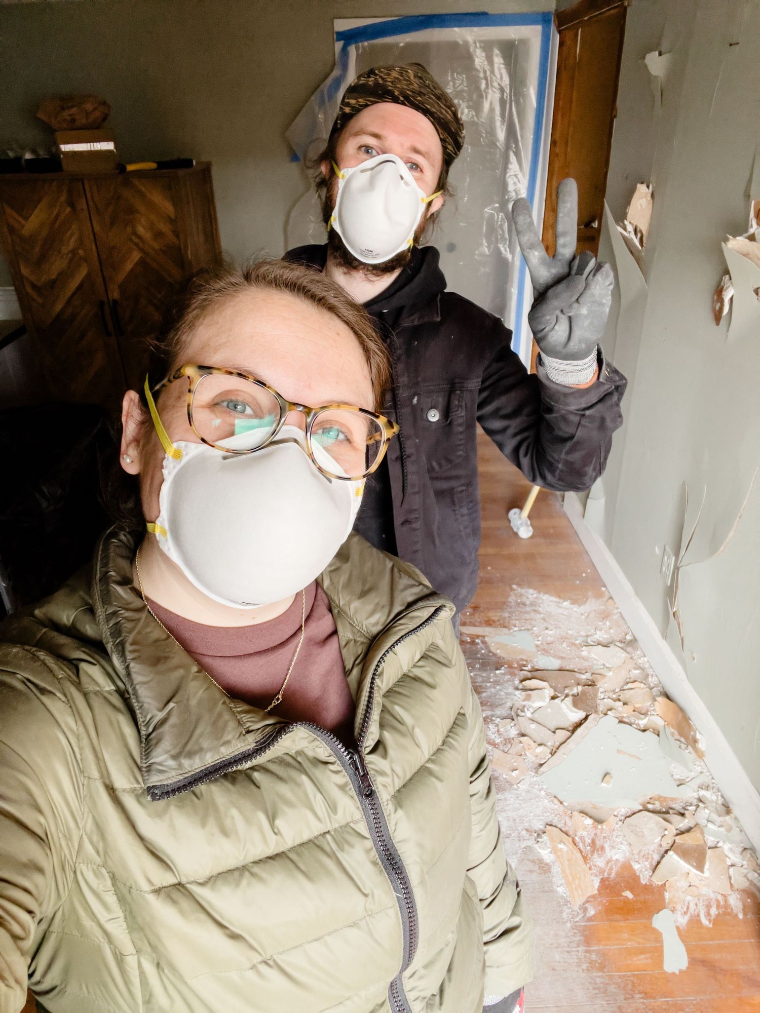 Two people wearing protective masks and work clothes during a home renovation project with debris visible on the floor.