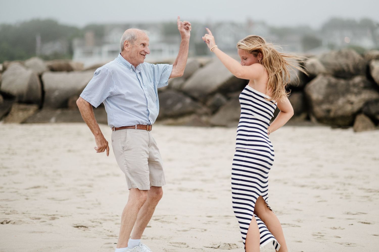 People in casual clothes playing and dancing together on sandy beach.