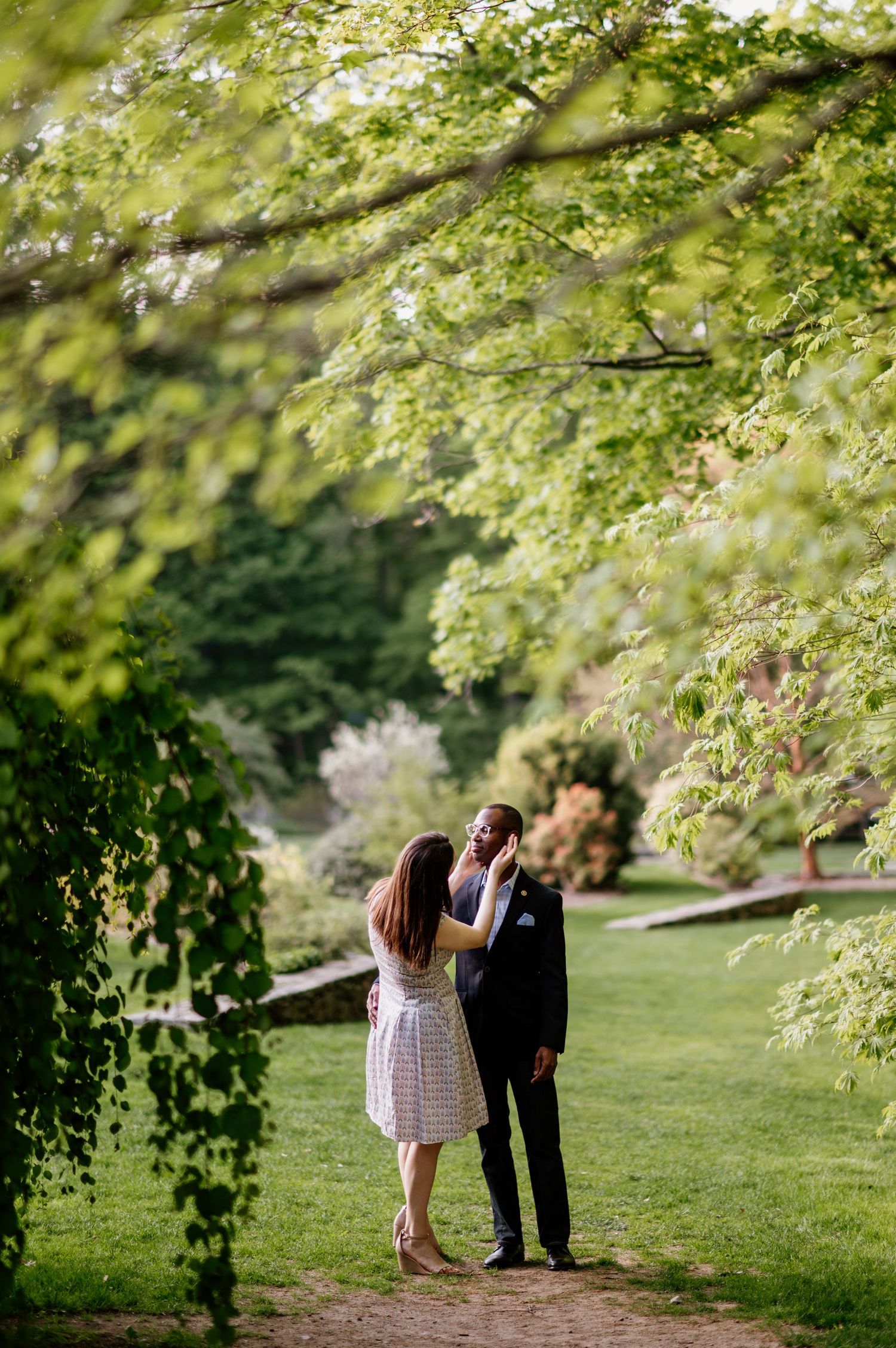 A romantic couple shares an intimate moment under blooming spring trees in a lush garden setting.