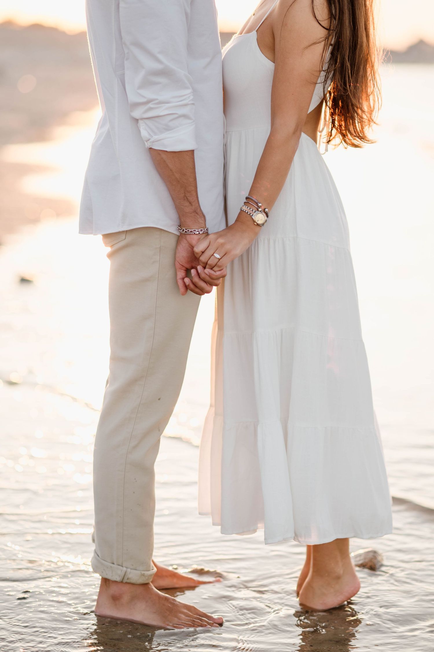 Feet of a couple standing in shallow ocean water during golden hour.