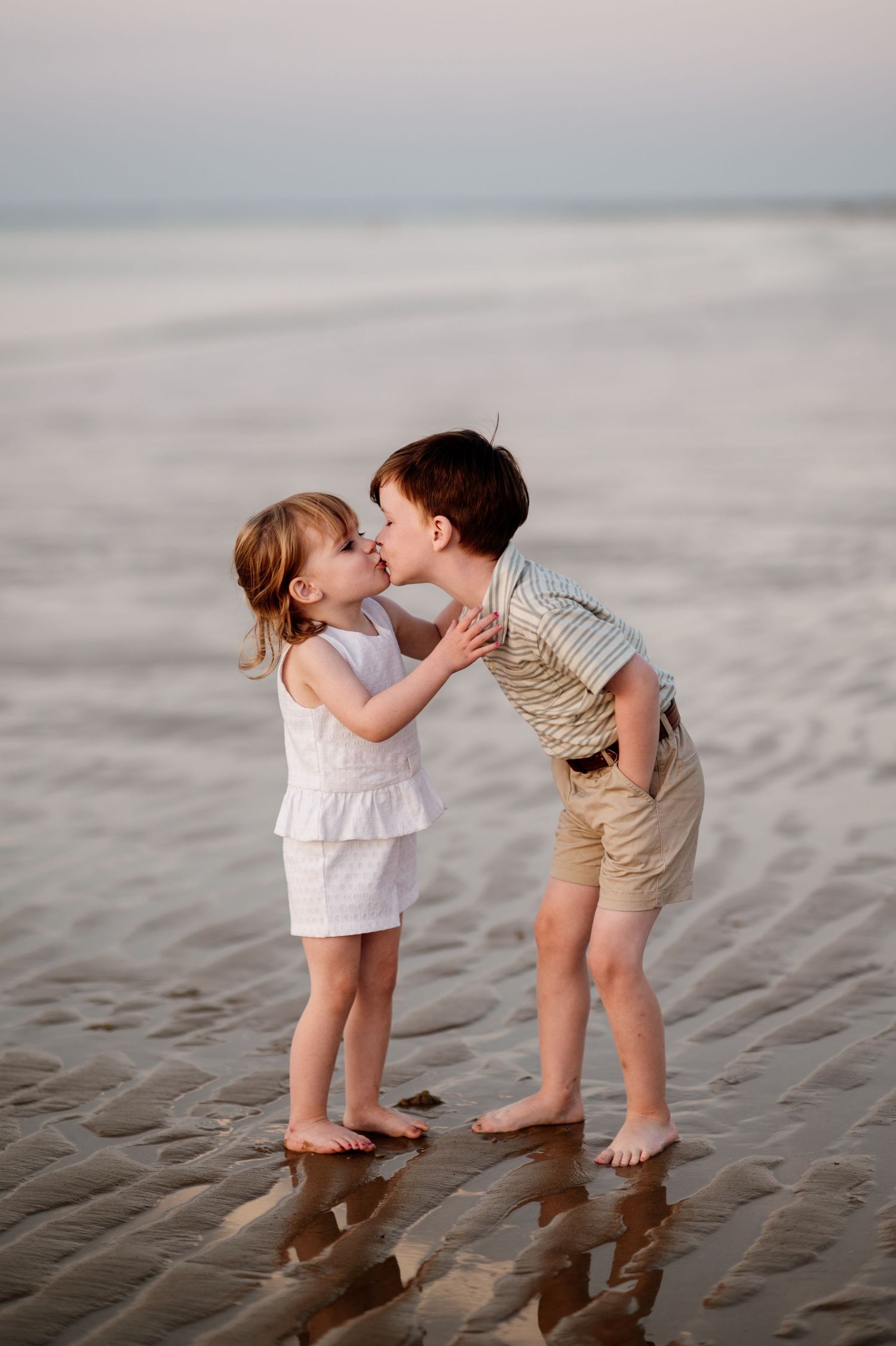 Two small children share a sweet moment while playing in the wet sand at the beach.