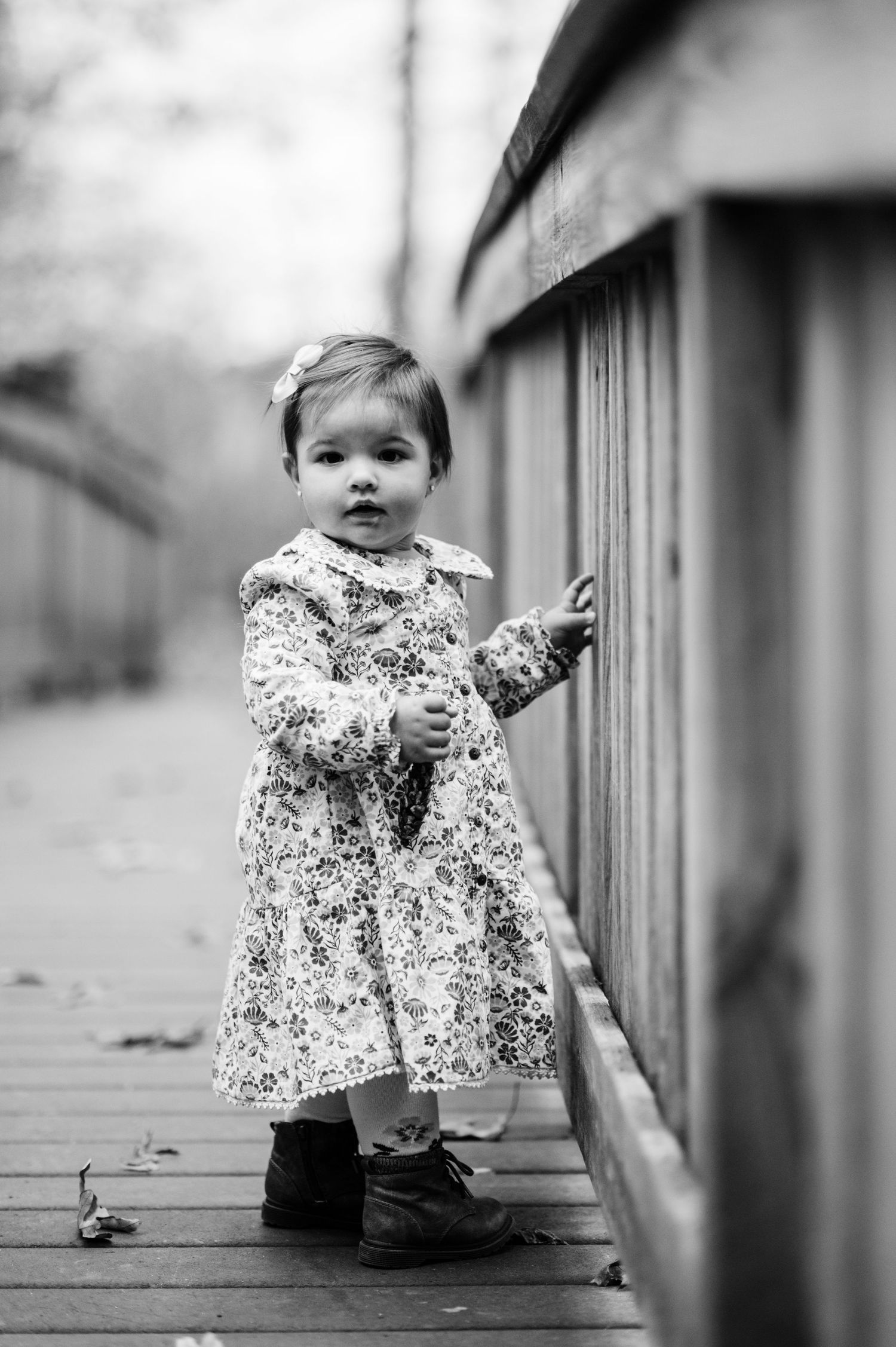 Small child in floral dress sitting on wooden deck railing.