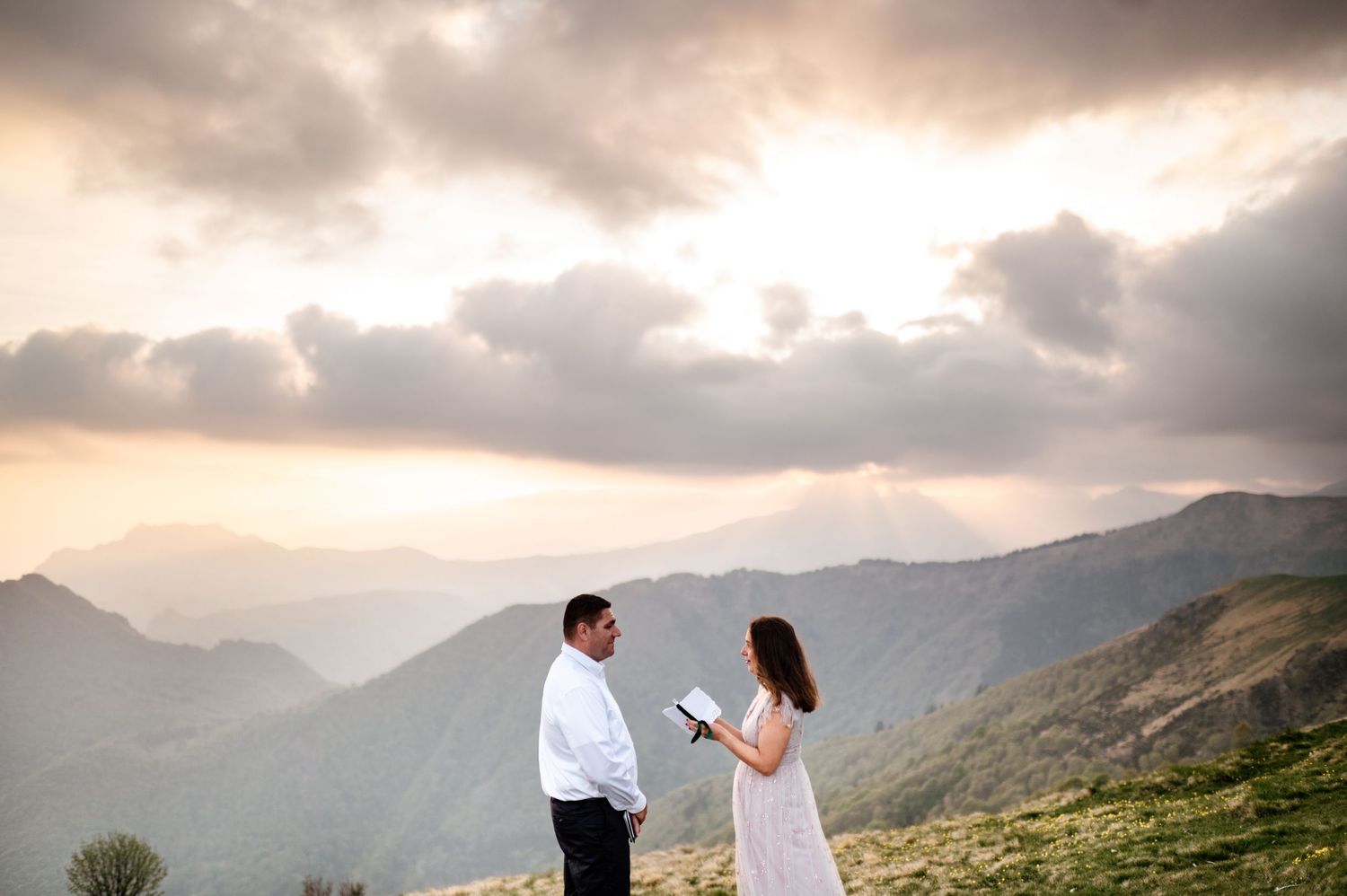 A couple stands silhouetted against dramatic mountain vistas during sunset.