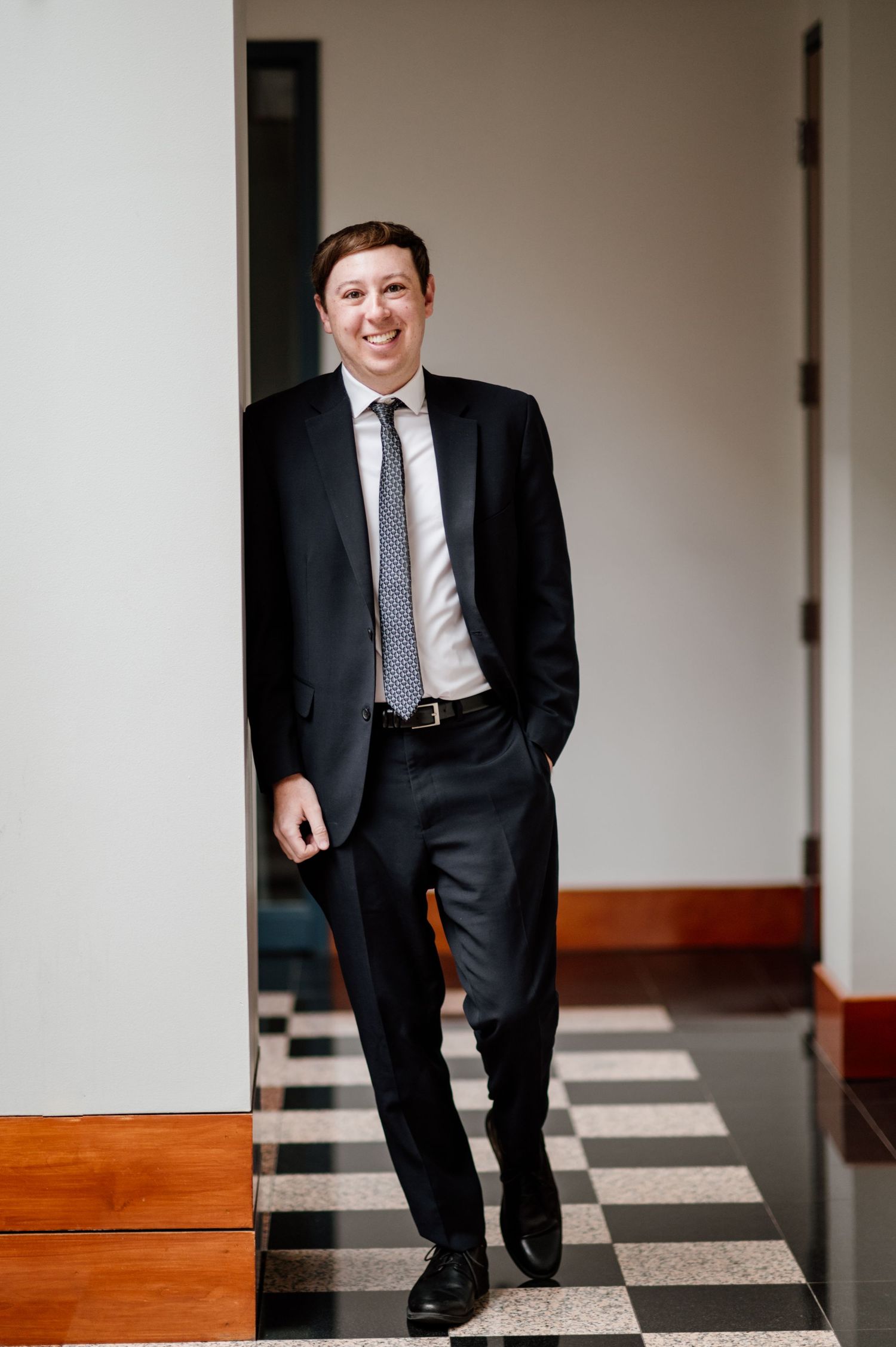 Professional portrait series showing black suit against white interior with checkered floor pattern.