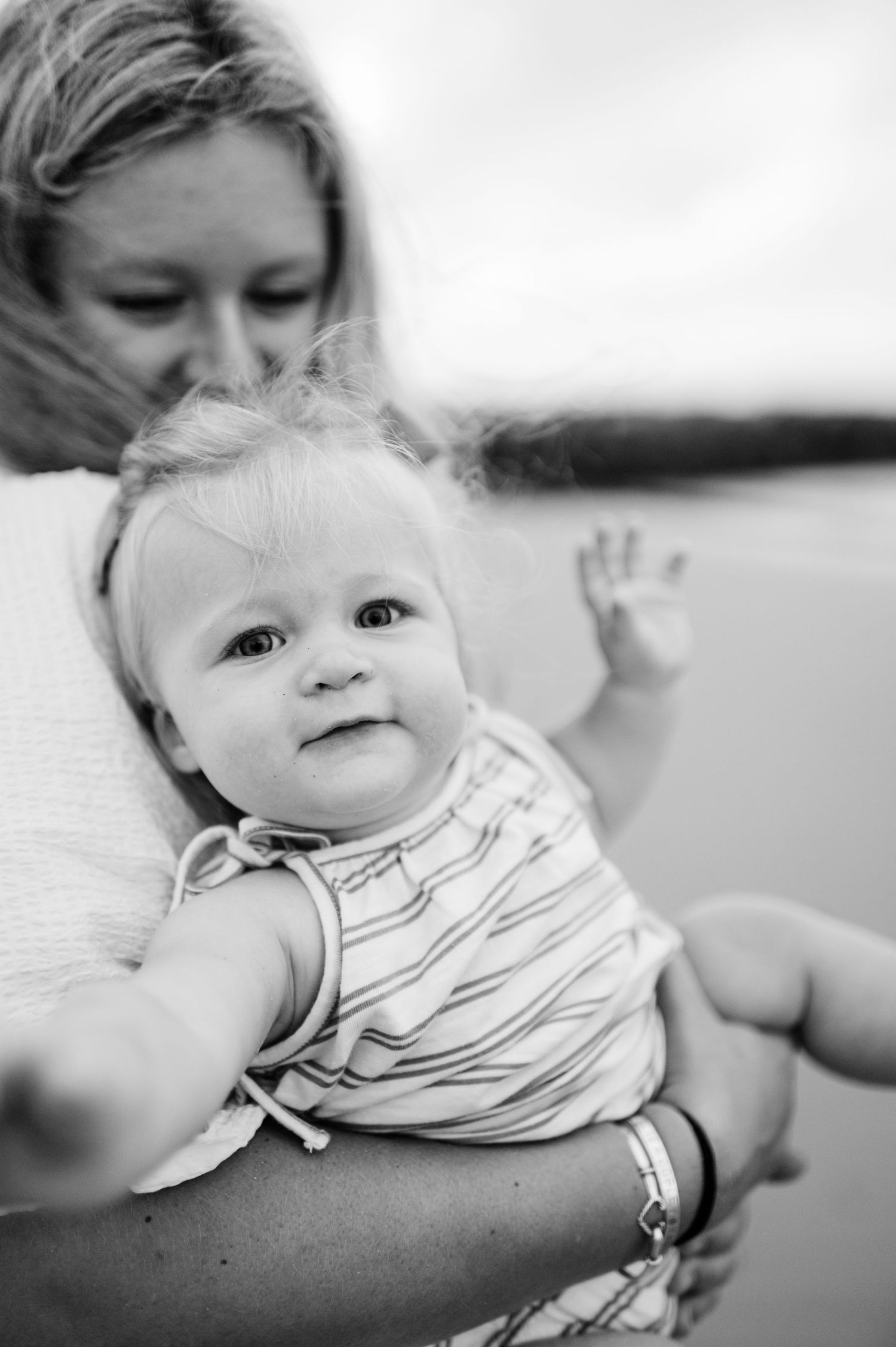 Black and white portrait of a smiling baby in a striped outfit being held against a blurred background.
