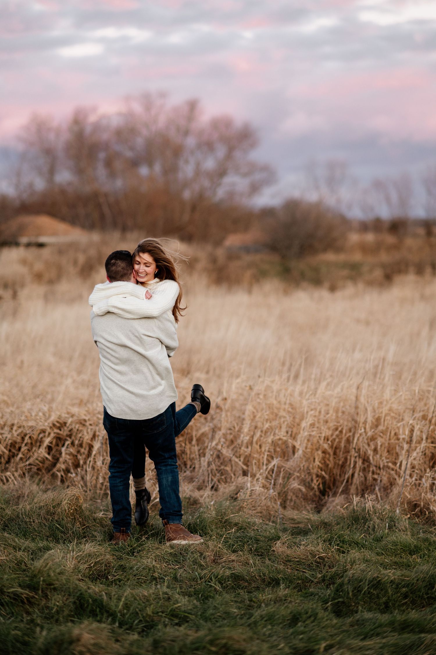 A romantic embrace in a golden field during sunset with moody pink skies.