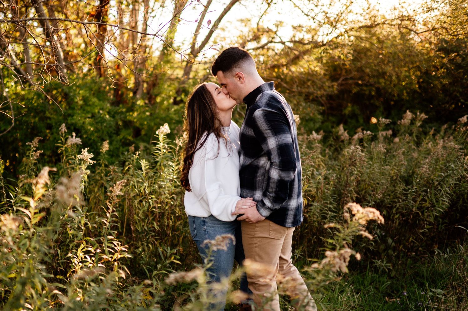 A couple shares a romantic moment in a golden sunlit field during sunset.