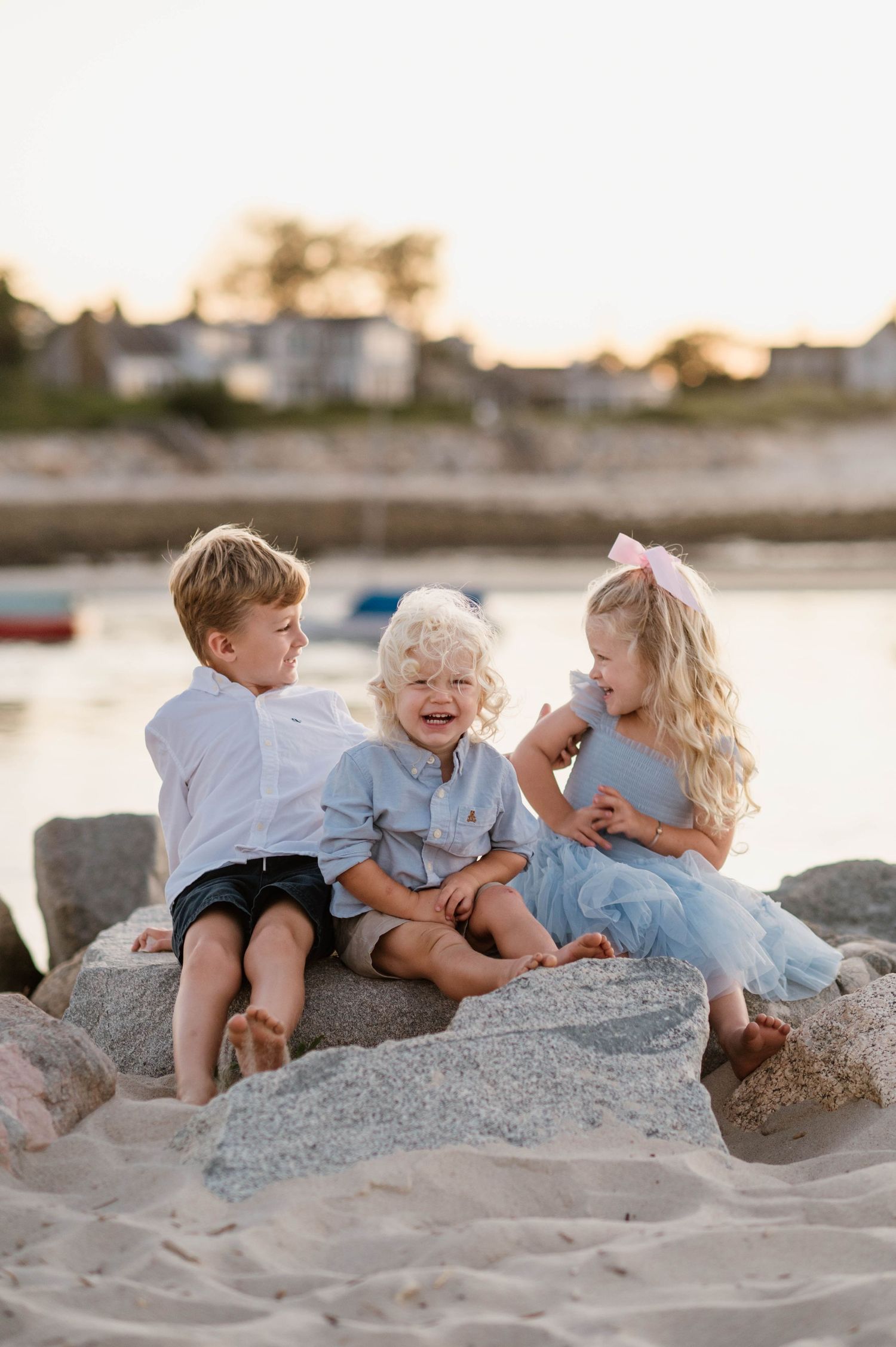 Children in light colored clothing playing and laughing together on coastal rocks at sunset.