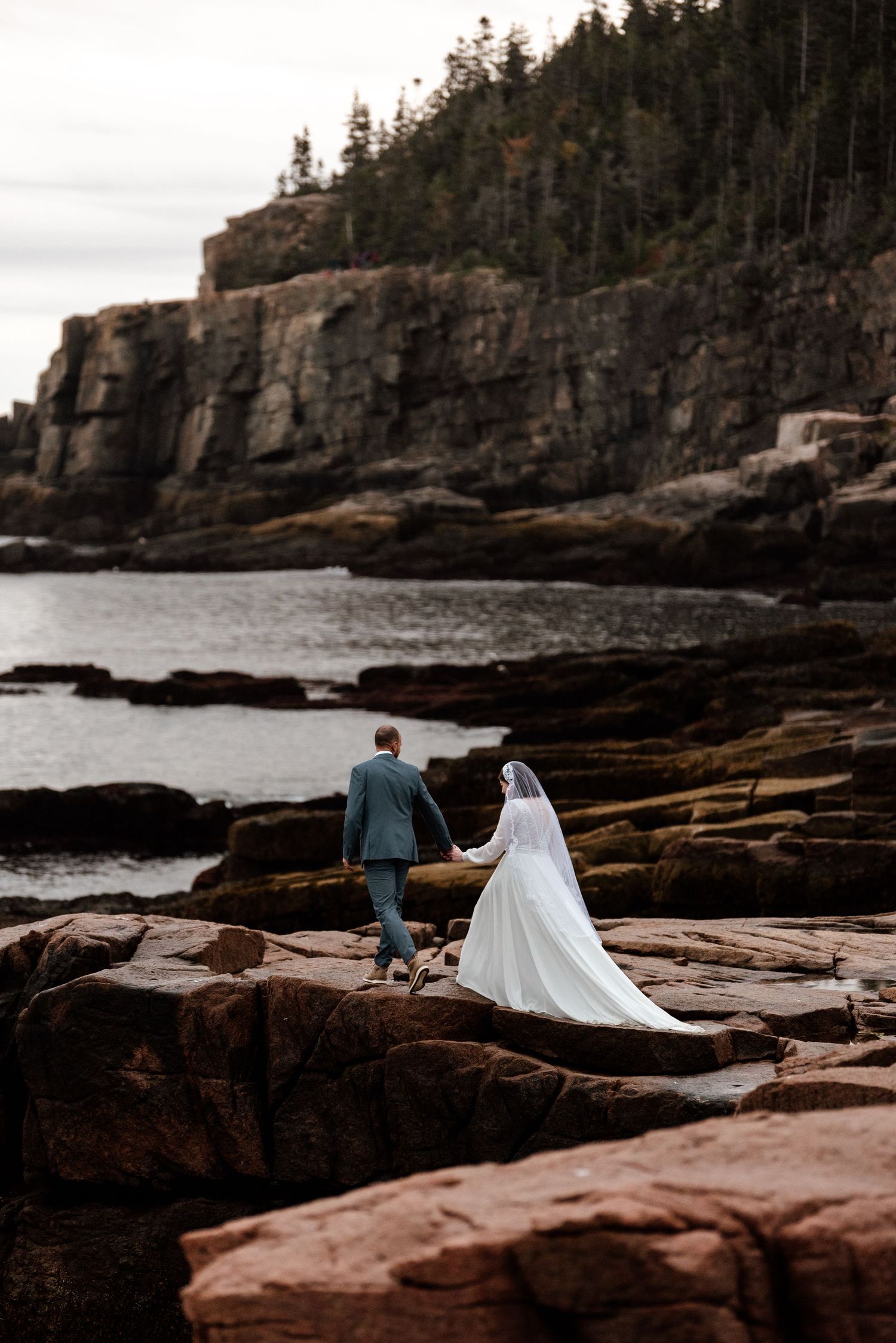 A dramatic coastal wedding photoshoot on rugged cliffs overlooking the ocean at sunset.