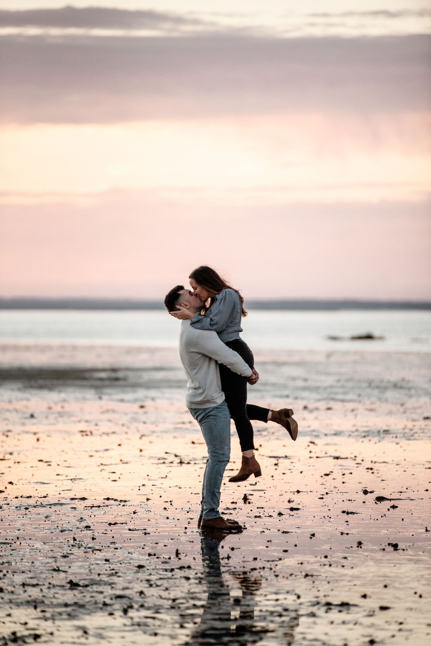 A couple embraces and lifts each other on a beach at sunset creating silhouettes against the sky.