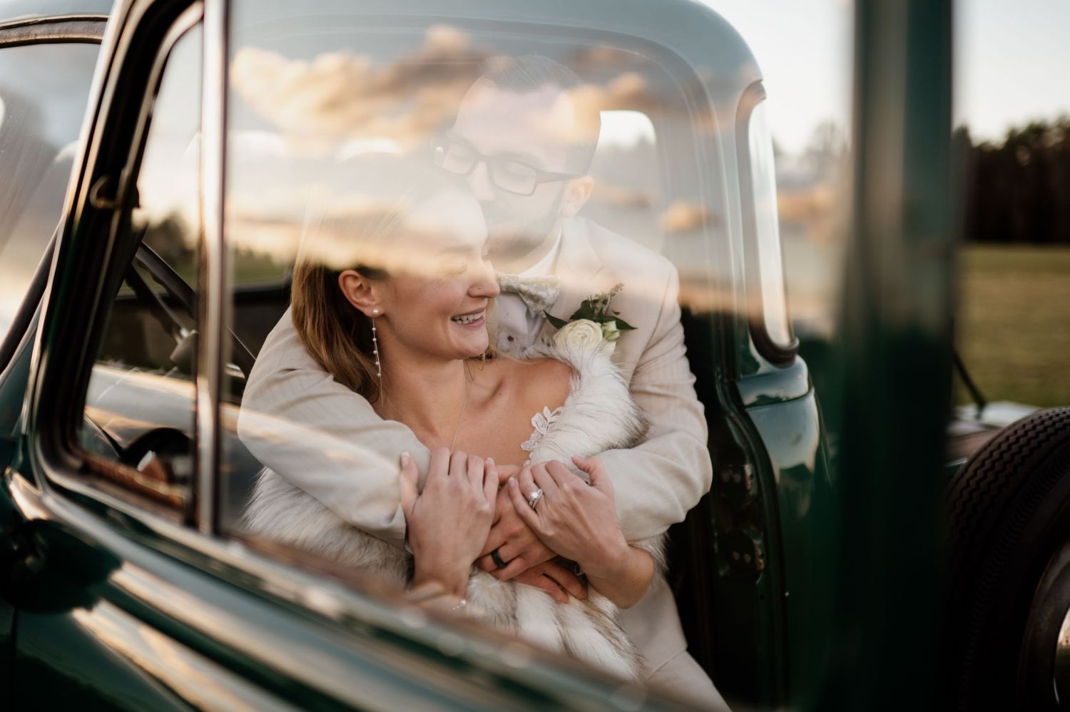 A couple shares a tender kiss in the backseat of a vintage car during golden hour lighting.