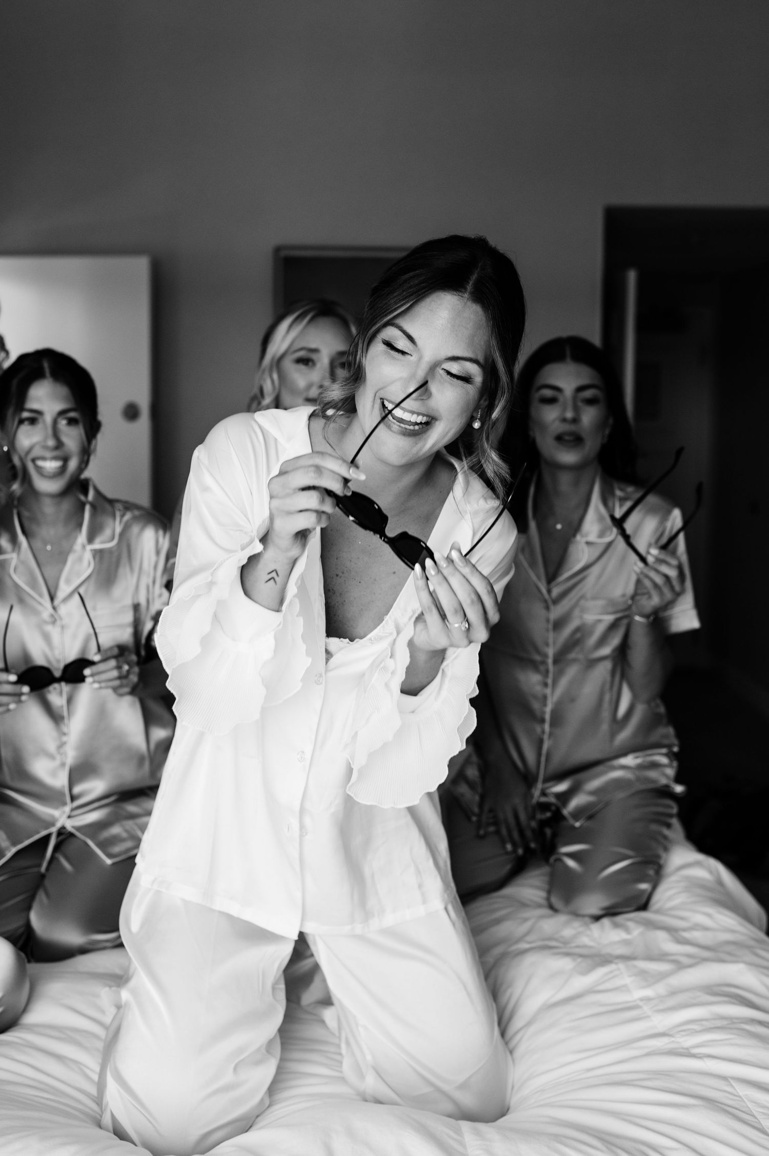 Group of friends in matching pajamas laugh and celebrate during a wedding morning get-ready session.
