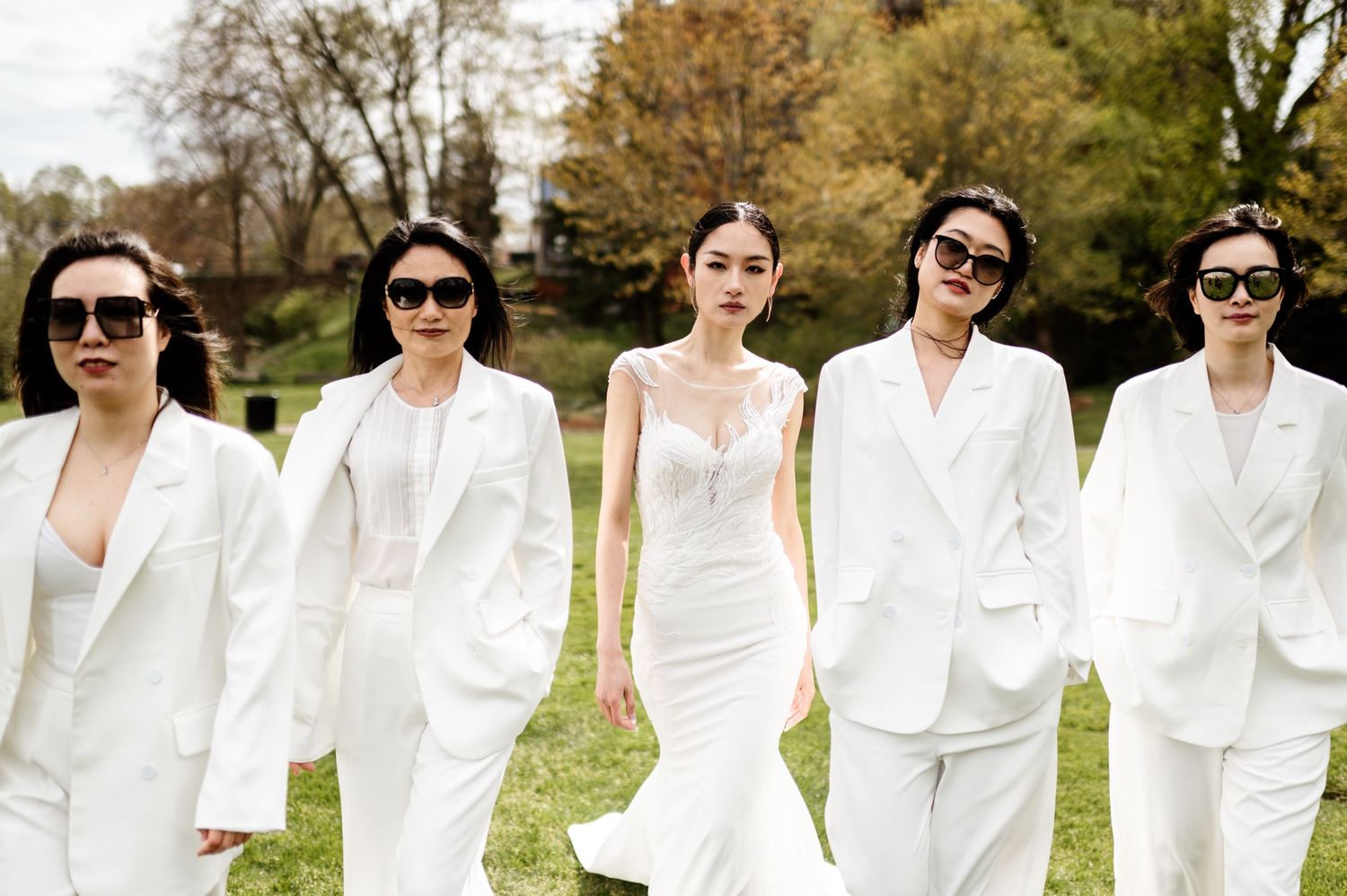 Group photo of wedding party members wearing white outfits in a garden setting.