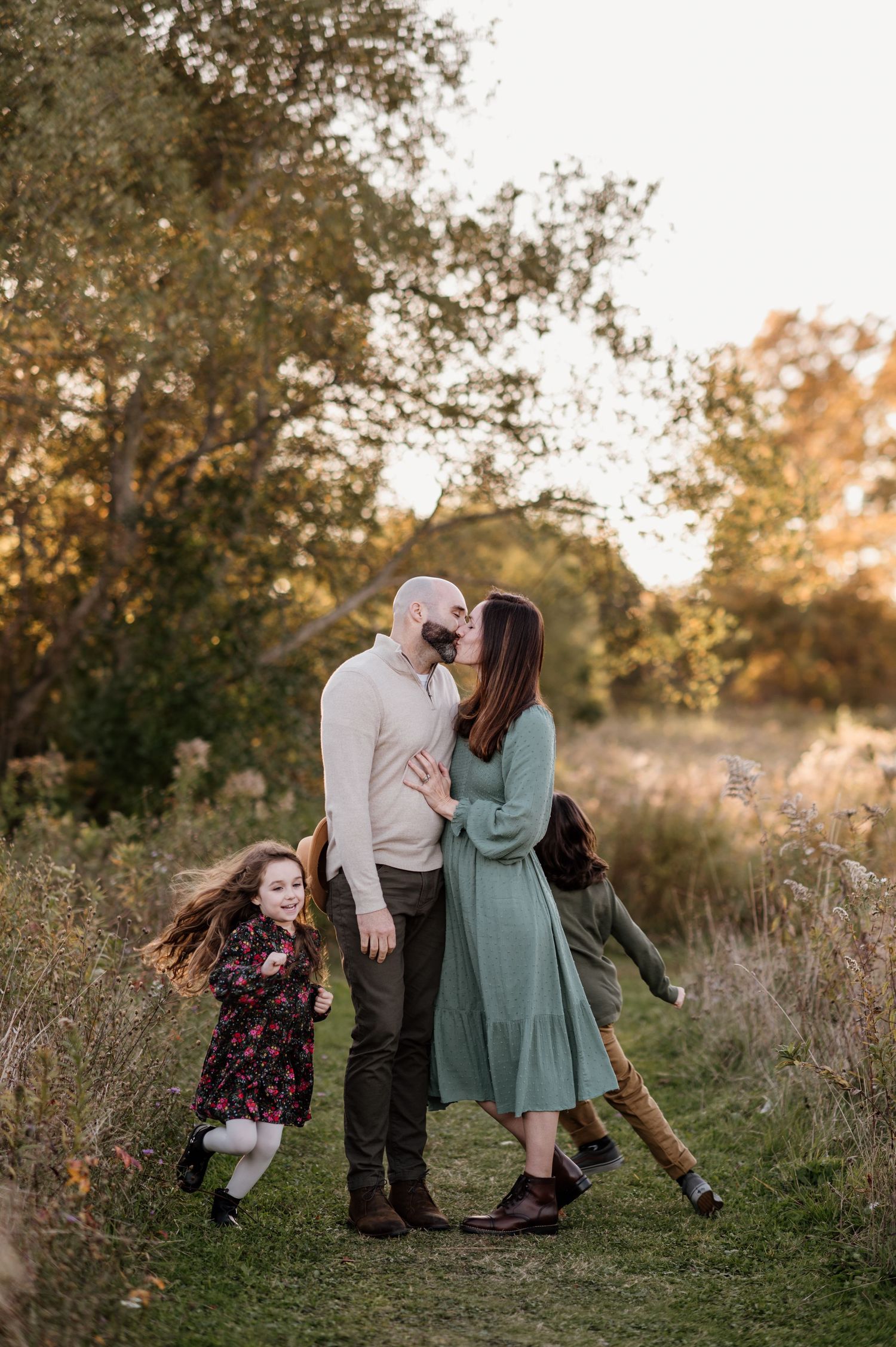 Playful family photoshoot in a golden field during sunset with tall grass and natural lighting.