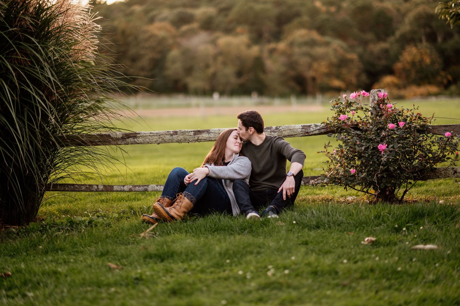Couple relaxing together on grassy hillside with flowering bushes at sunset.