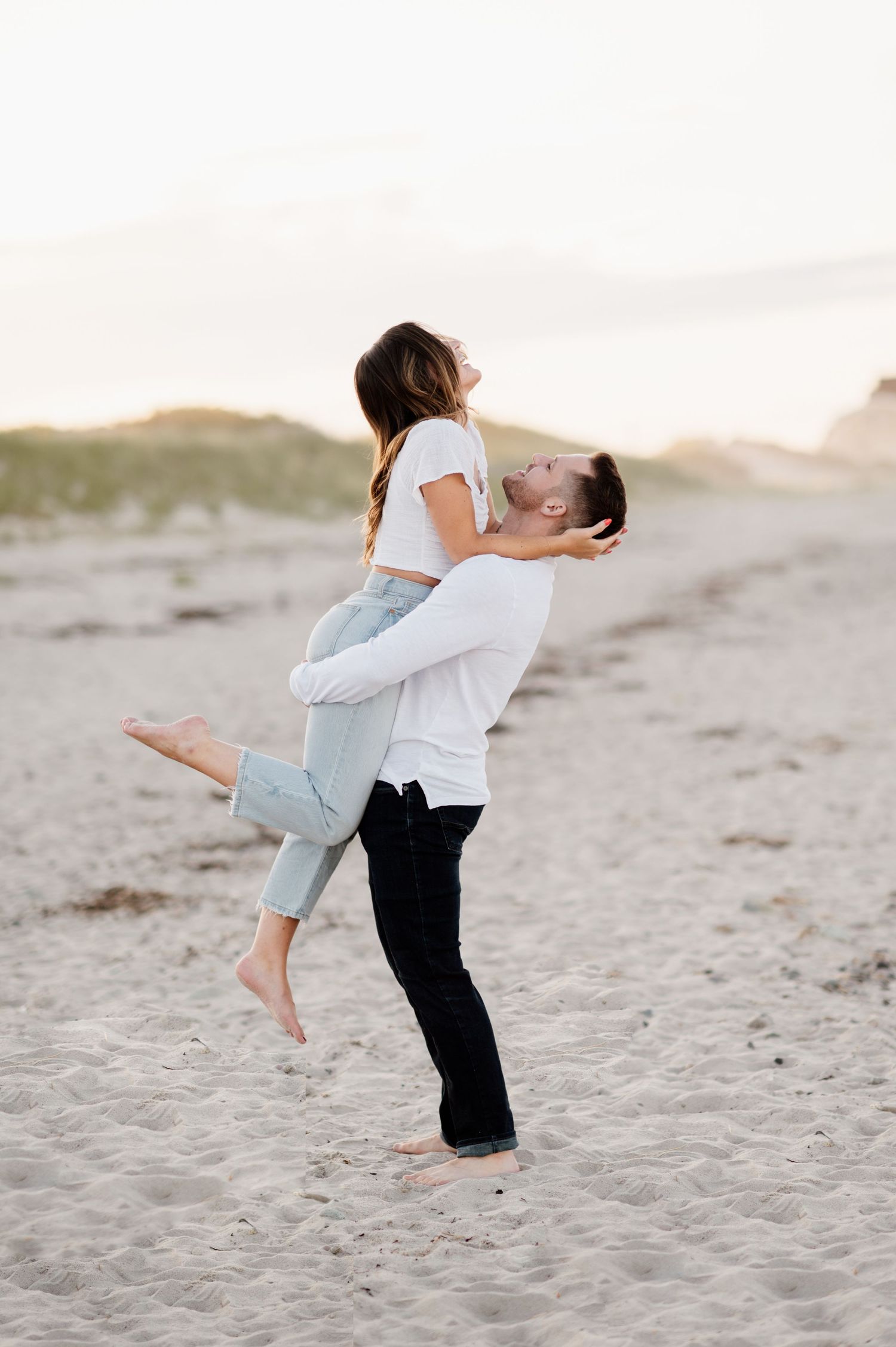 A romantic moment captured on the beach as a couple embraces in a playful lift at sunset.