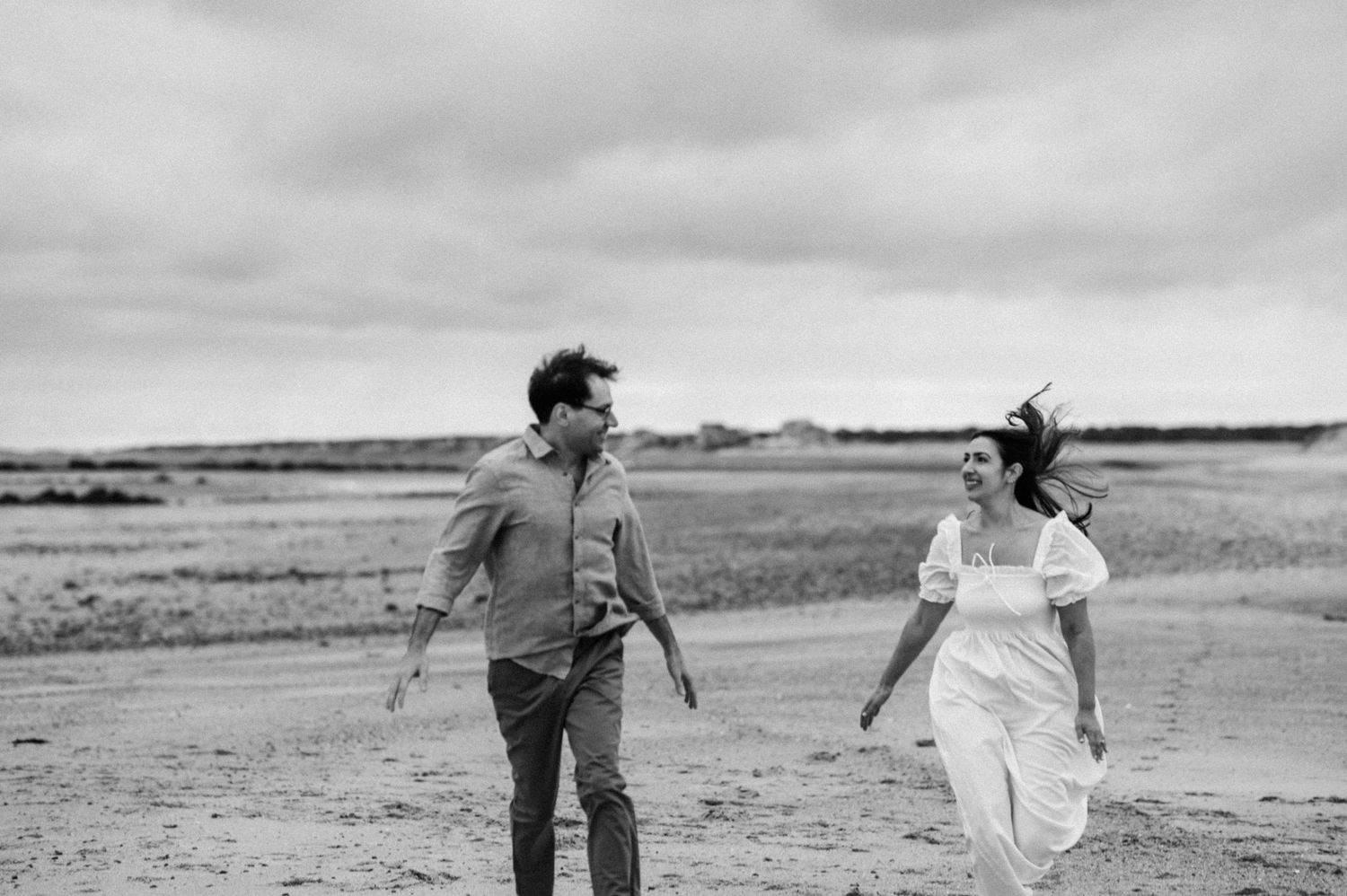 Couple walking and playing together on a scenic beach with dramatic cloudy skies.