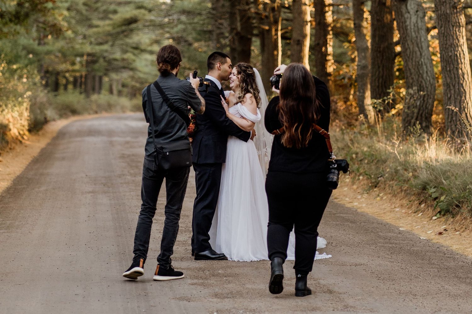 A couple shares an intimate moment on a tree-lined dirt path during a romantic outdoor photo session.
