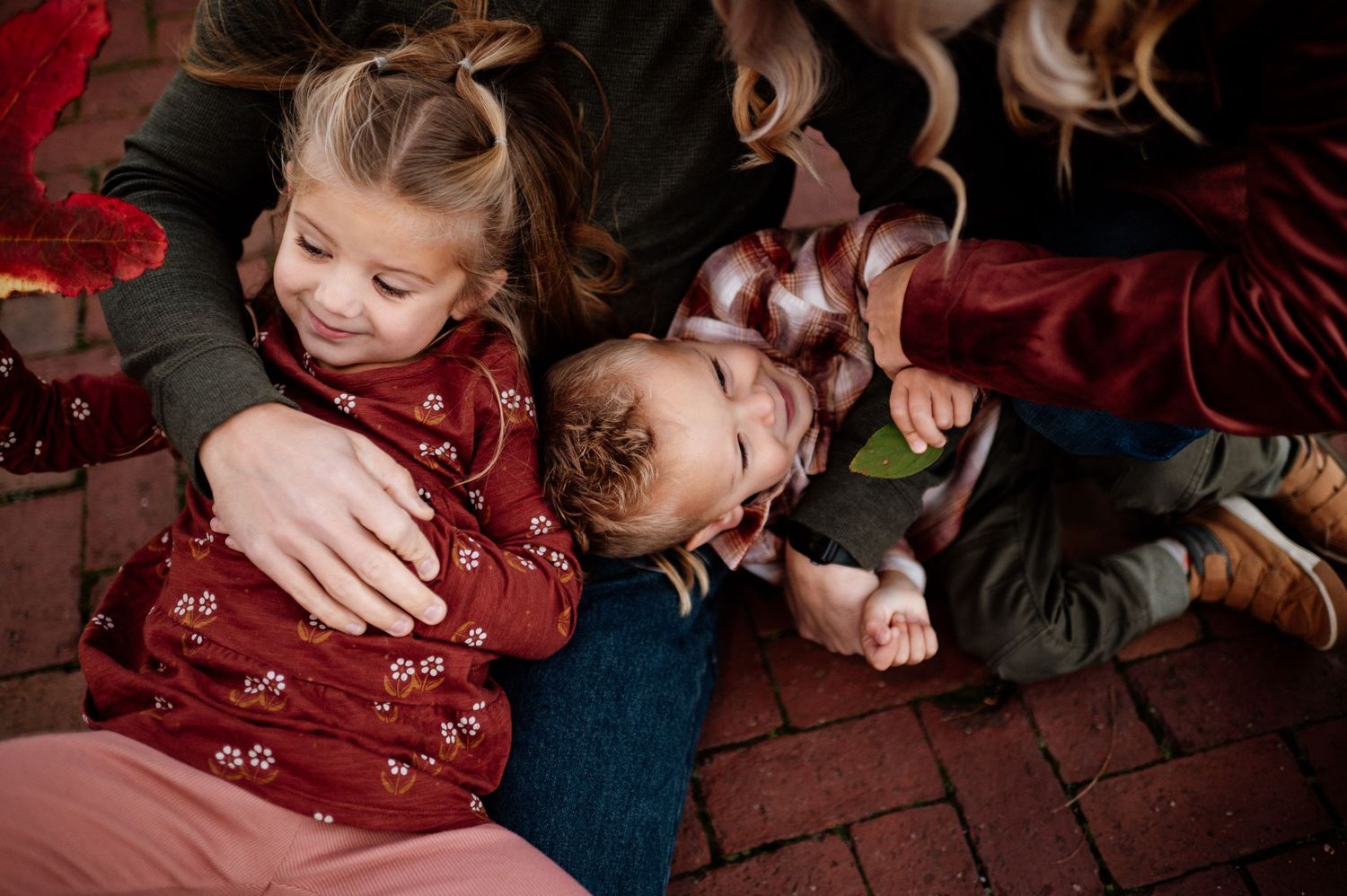 Children playing and embracing on a red brick surface in warm tones.