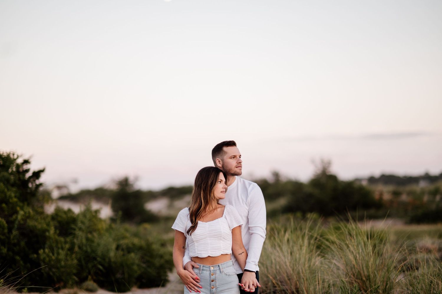 Couple embracing in casual white outfits against a natural outdoor backdrop.