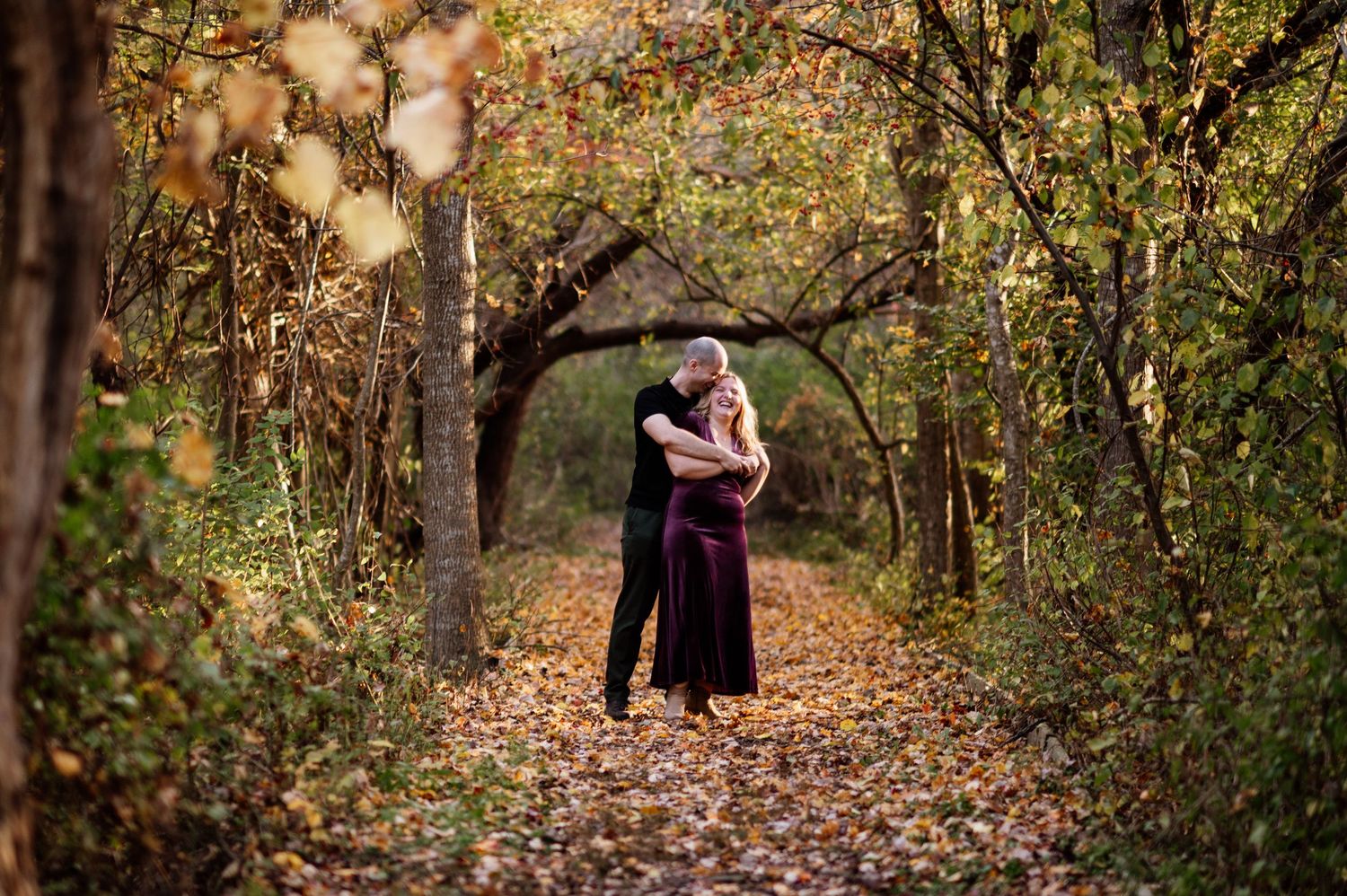 A romantic autumn engagement photoshoot in a wooded path with golden falling leaves.