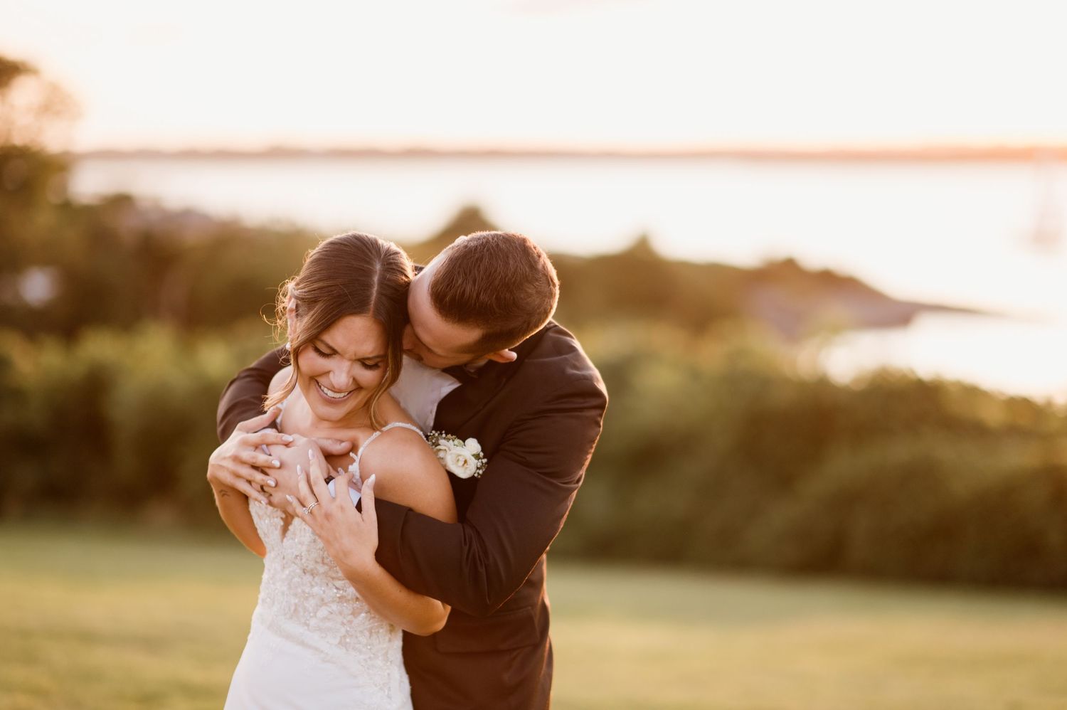 A couple embraces during golden hour in a grassy field with warm sunlight creating a romantic silhouette.