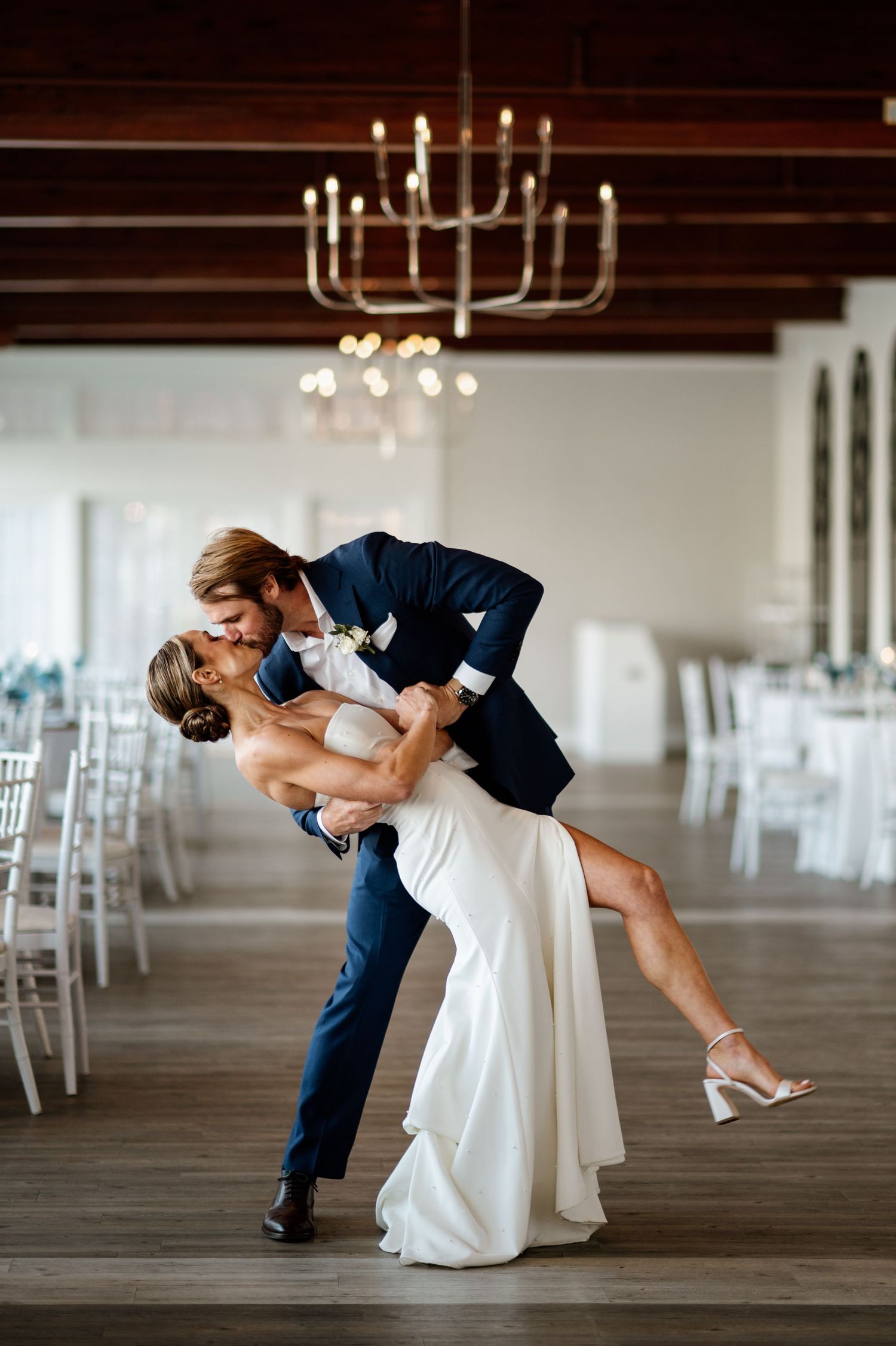 Dramatic dip dance move performed in an elegant white reception hall with chandeliers.