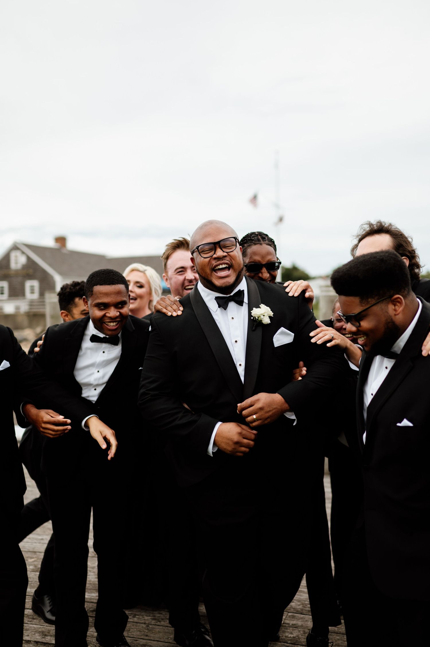 Groomsmen in black tuxedos sharing laughs and embraces during wedding photo session.