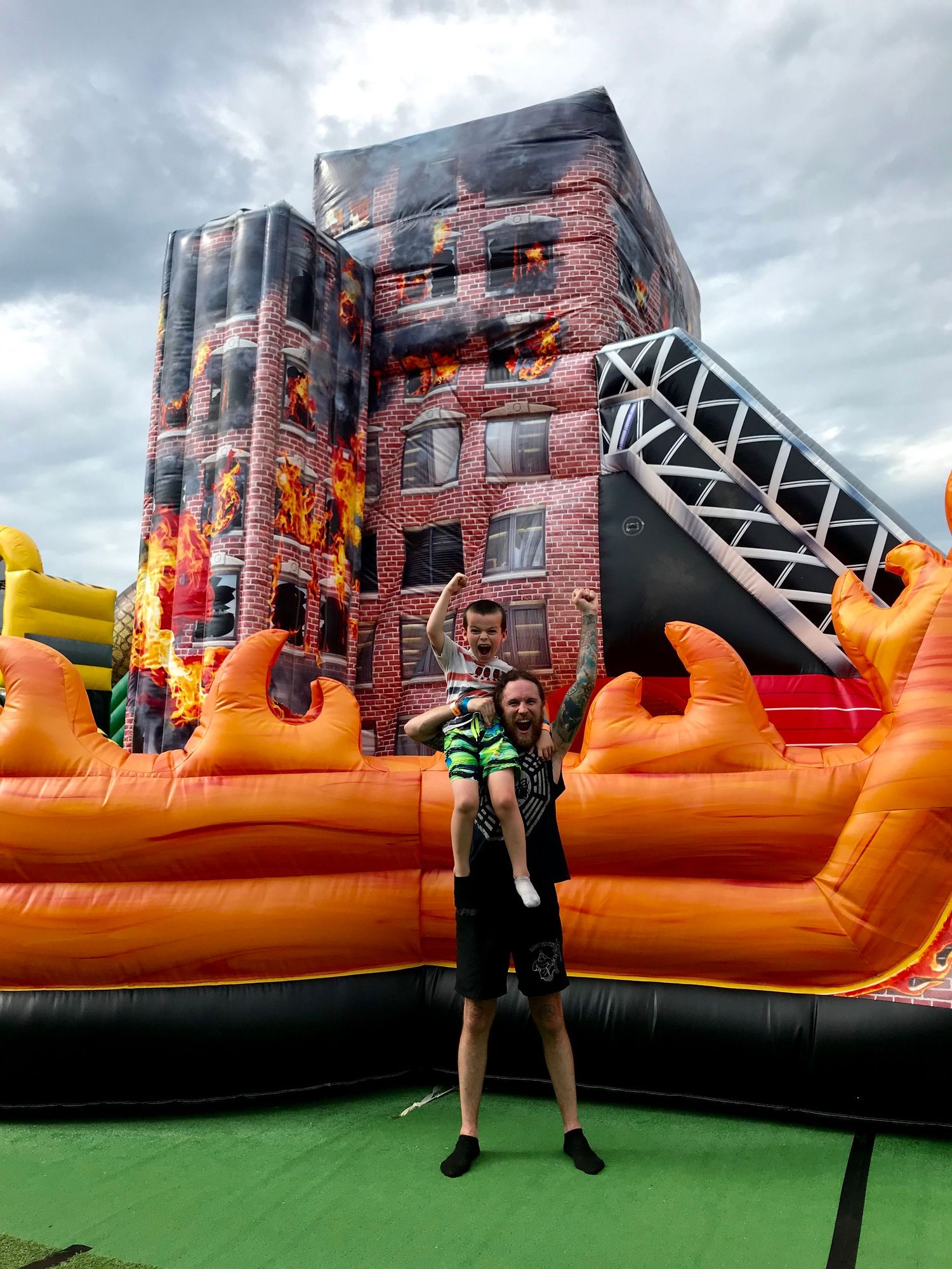 People enjoying a large orange inflatable obstacle course with climbing walls under cloudy skies.