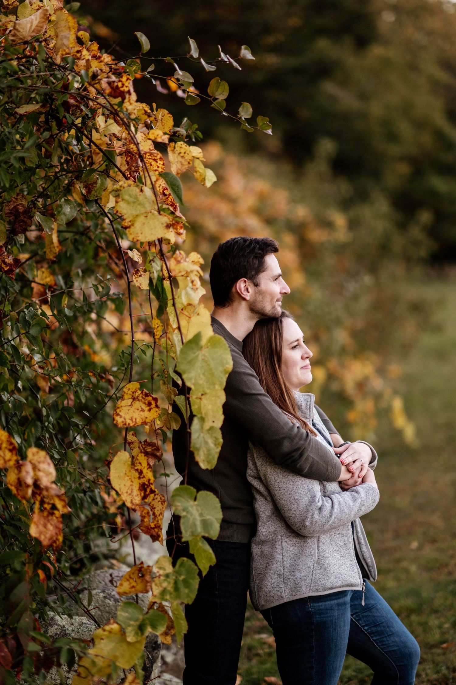 Couple embracing in autumn vineyard with golden leaves and warm sunlight creating romantic atmosphere.