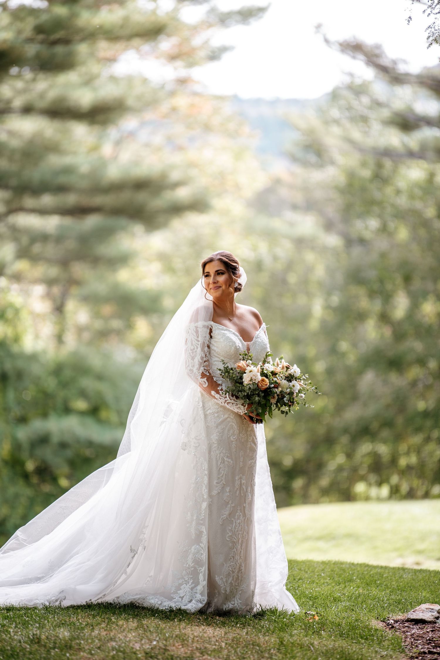 Bride in flowing lace gown poses gracefully in a sunlit garden setting.