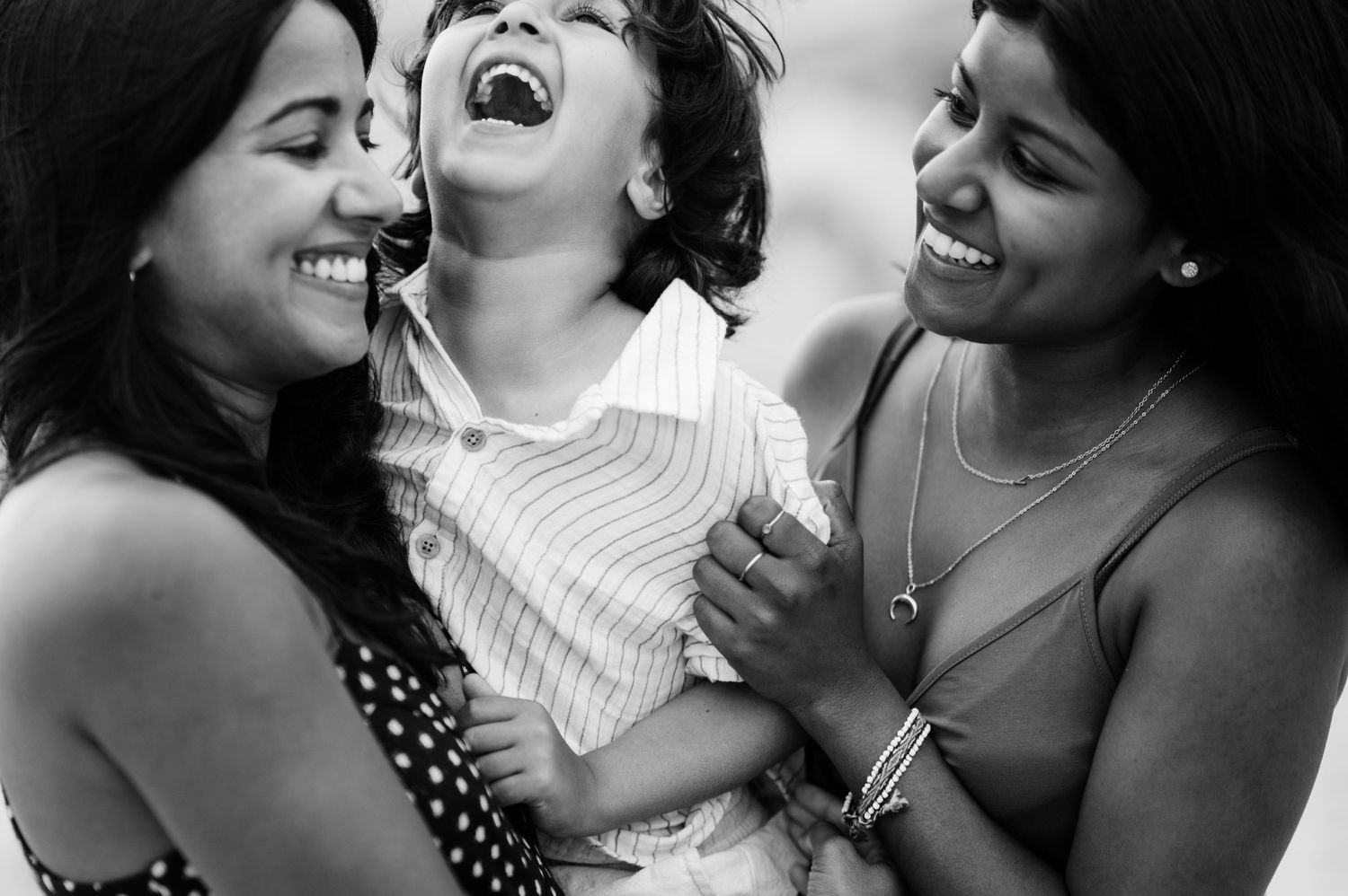 A candid black and white photograph captures three people sharing a joyful moment of genuine laughter together.