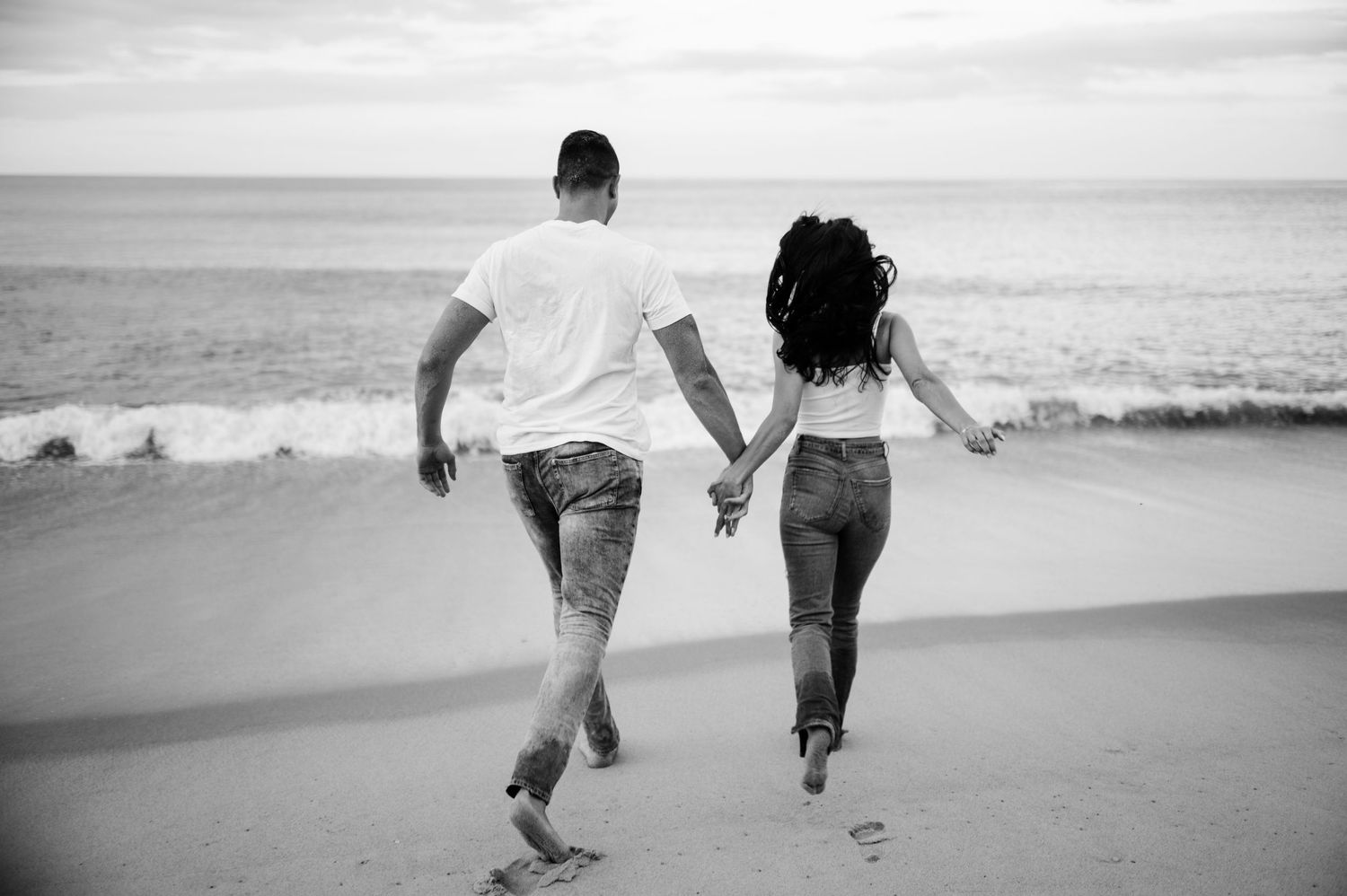 Black and white photo of couple walking together on beach shoreline.