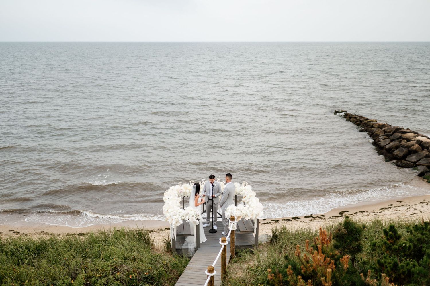 Scenic coastal beach view with a wooden pier extending into the gray waters under an overcast sky.
