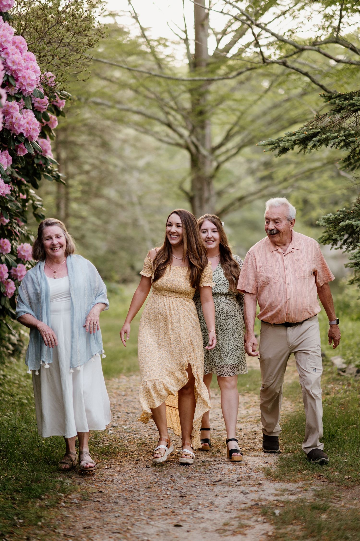 Family walking together on a tree-lined path with blooming pink rhododendrons.