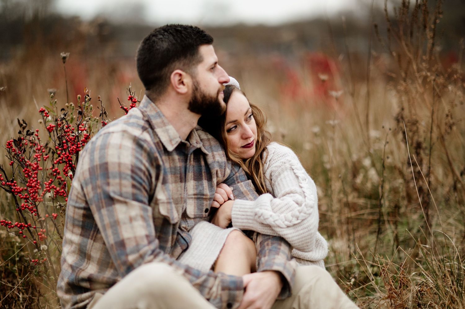 A romantic autumn moment in a field with red berries as a couple embraces in casual attire.