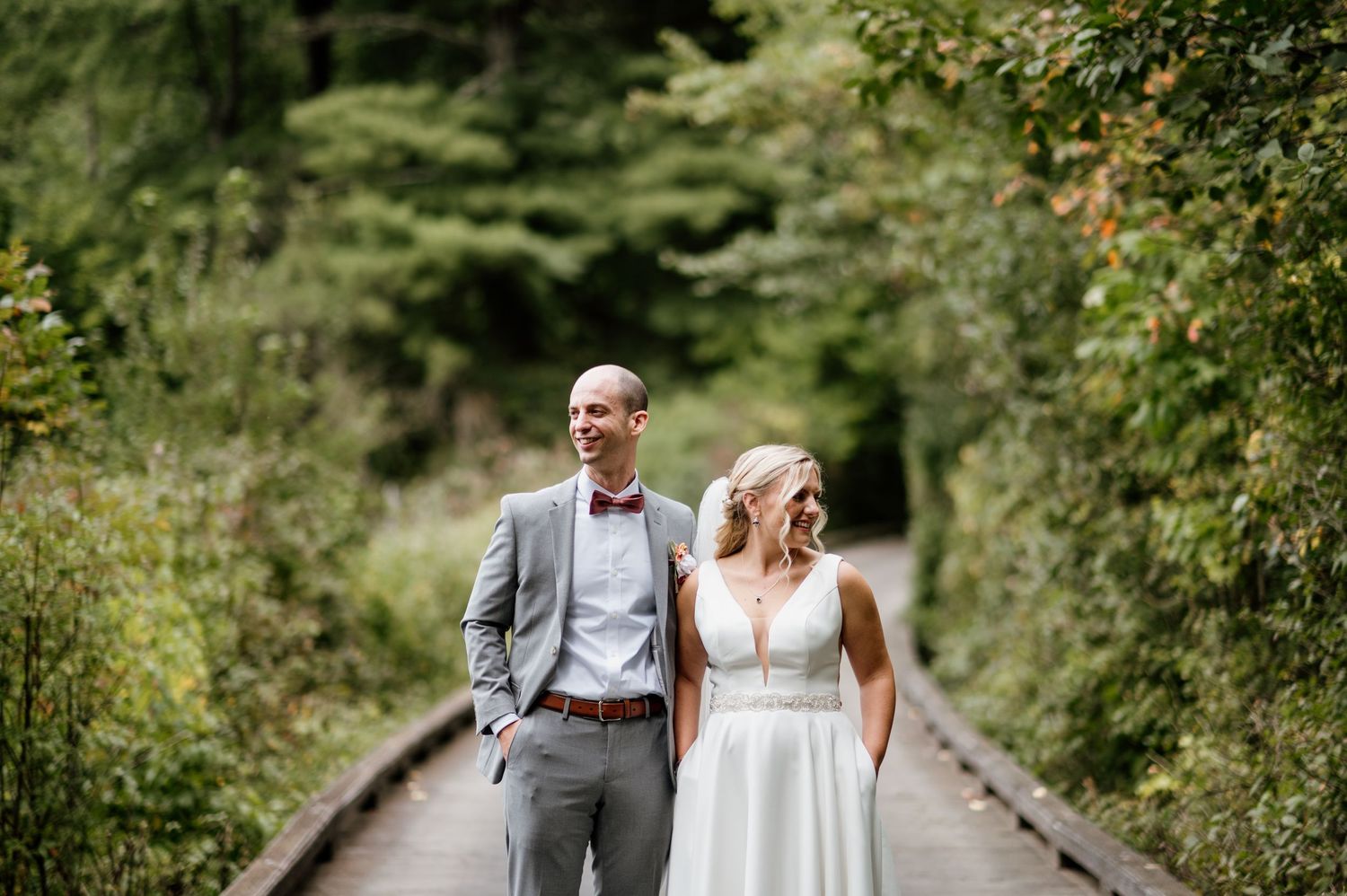 Couple strolls along a tree-lined garden path in wedding attire.