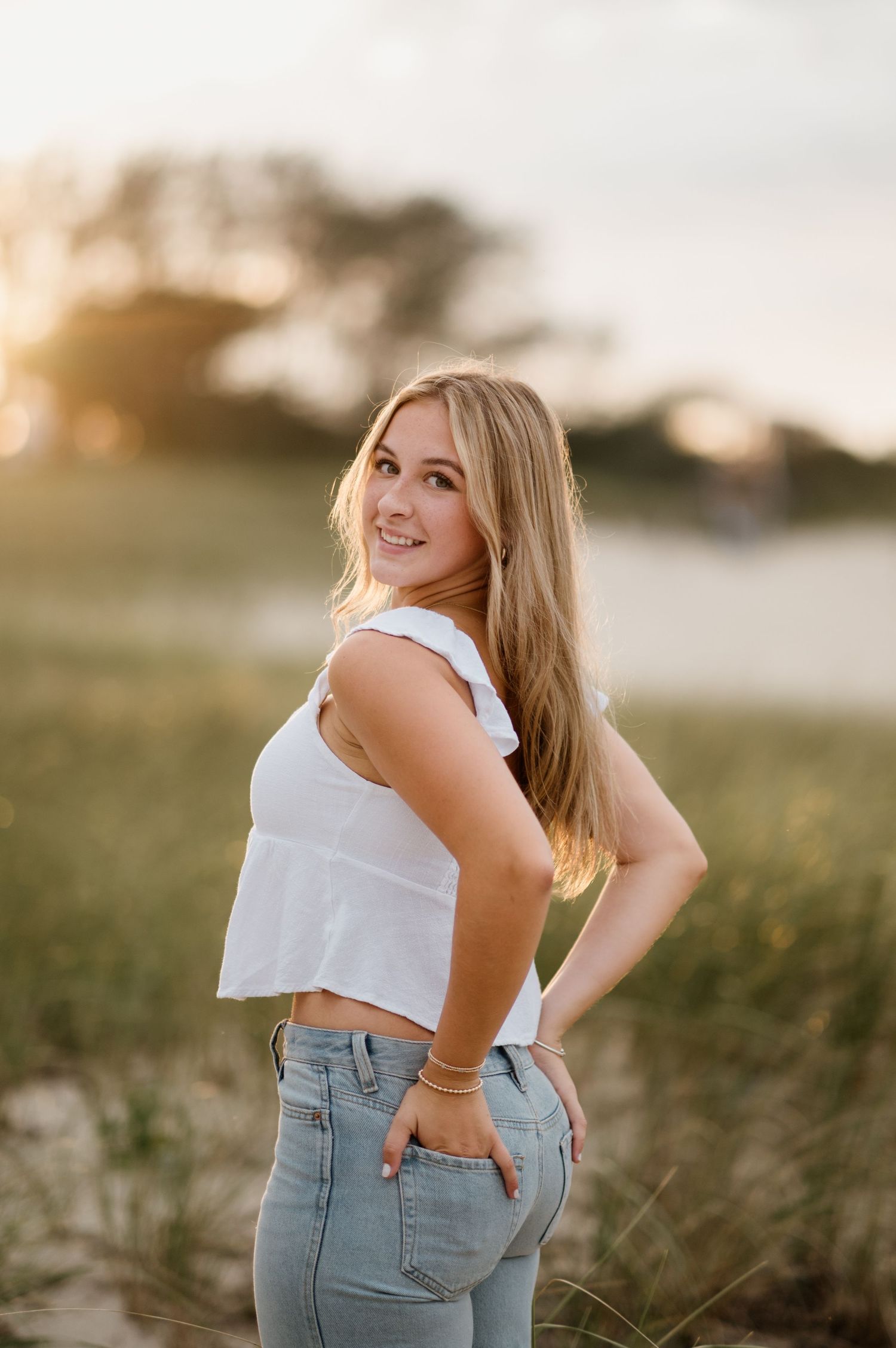 Portrait at sunset with white crop top and high-waisted jeans in a grassy outdoor setting during golden hour.