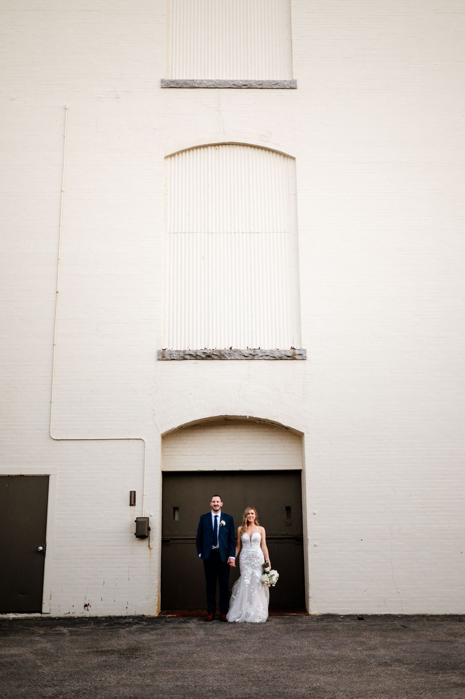 Minimalist wedding portrait against white brick wall with dramatic negative space.
