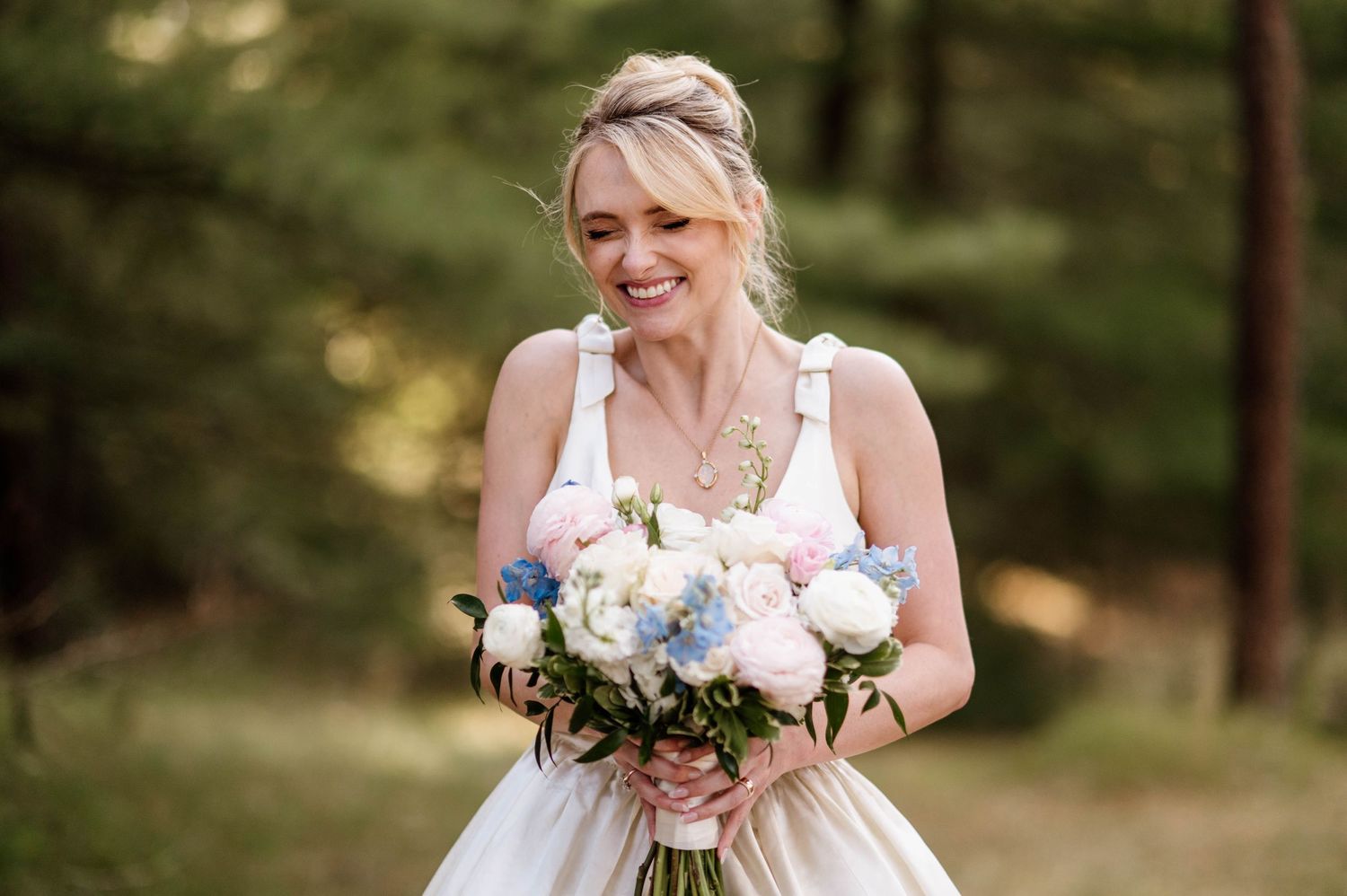 A bride in a white wedding dress holds a bouquet of flowers in an outdoor garden setting.
