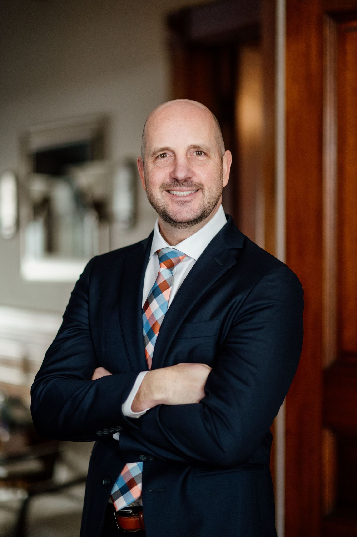 Professional portrait of a businessman in a navy suit and striped tie standing with arms crossed.